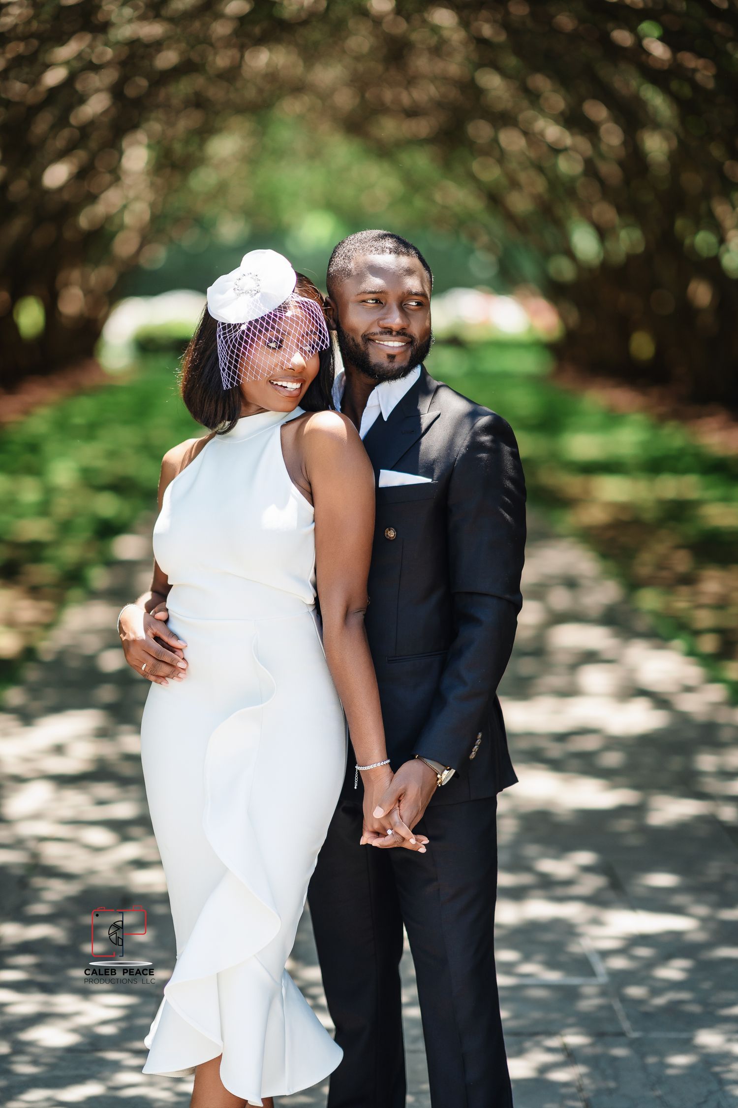 A couple in wedding attire share a joyful moment together outdoors under tree branches.