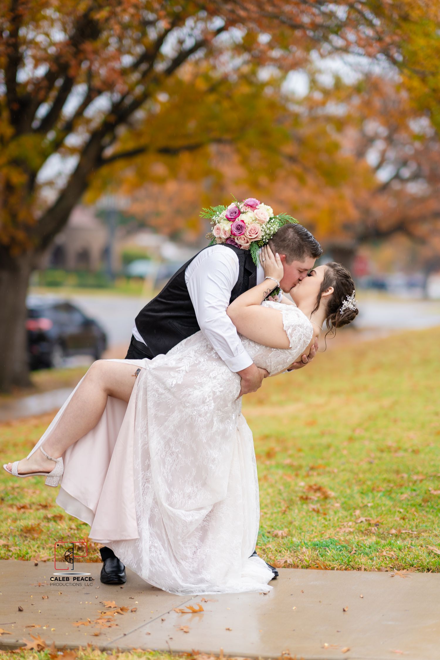 A romantic autumn wedding photo series shows a couple dipping and kissing on a path covered with fallen leaves.