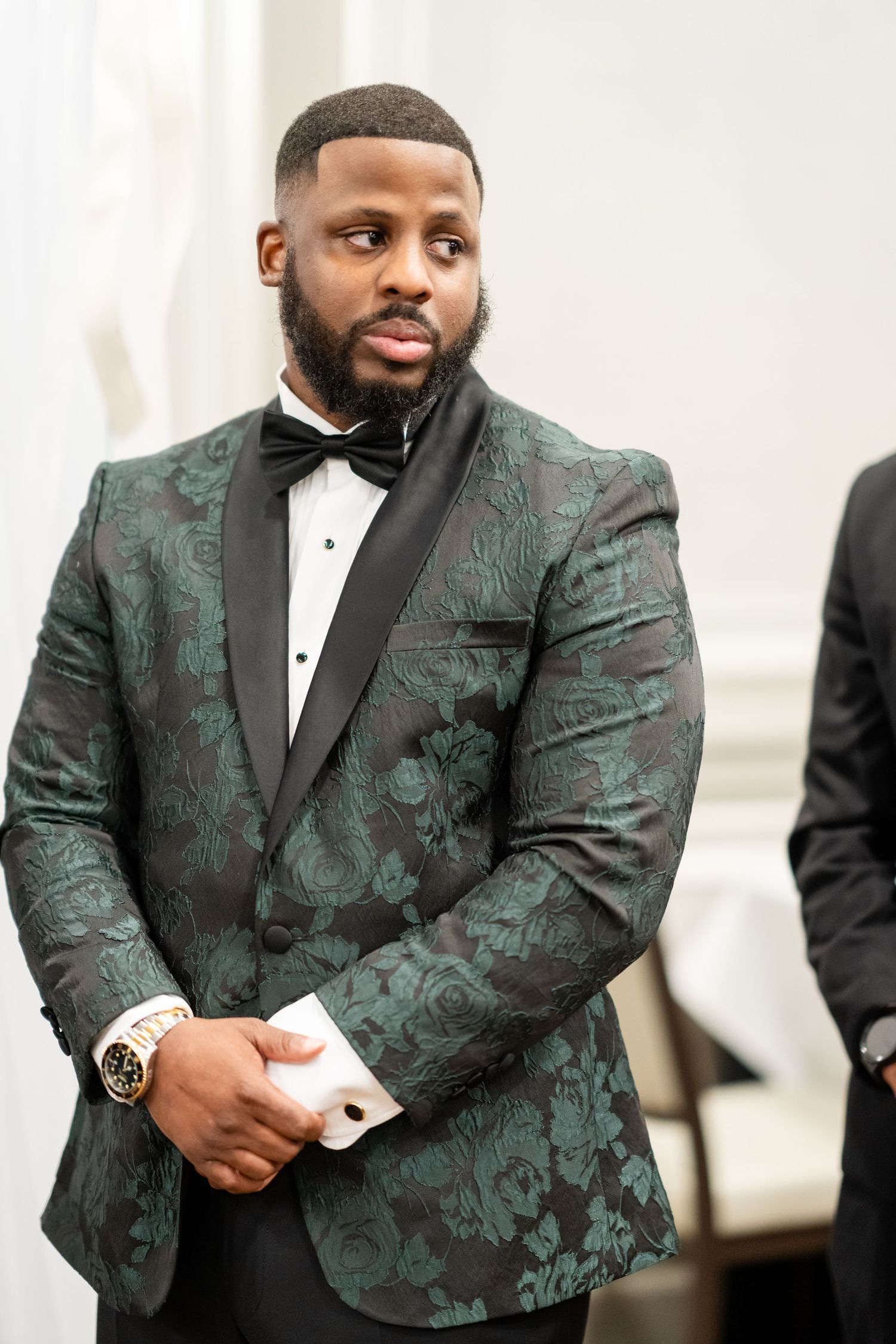 Groom wearing luxurious green patterned tuxedo jacket with black lapels and bow tie.