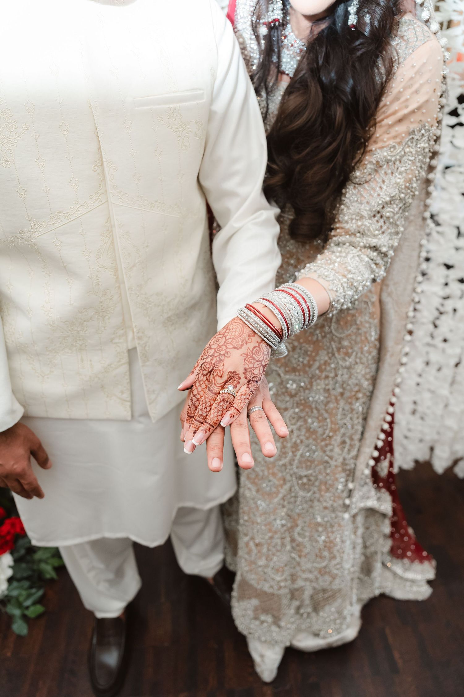 Couple in traditional wedding attire showing detailed henna design on hands.