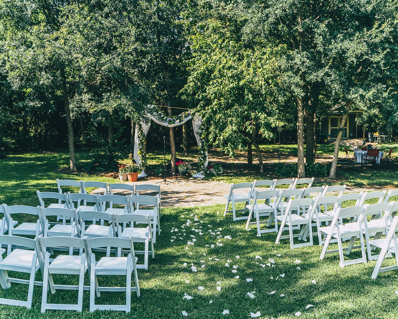 White folding chairs arranged in rows on a sunny lawn for an outdoor wedding ceremony.