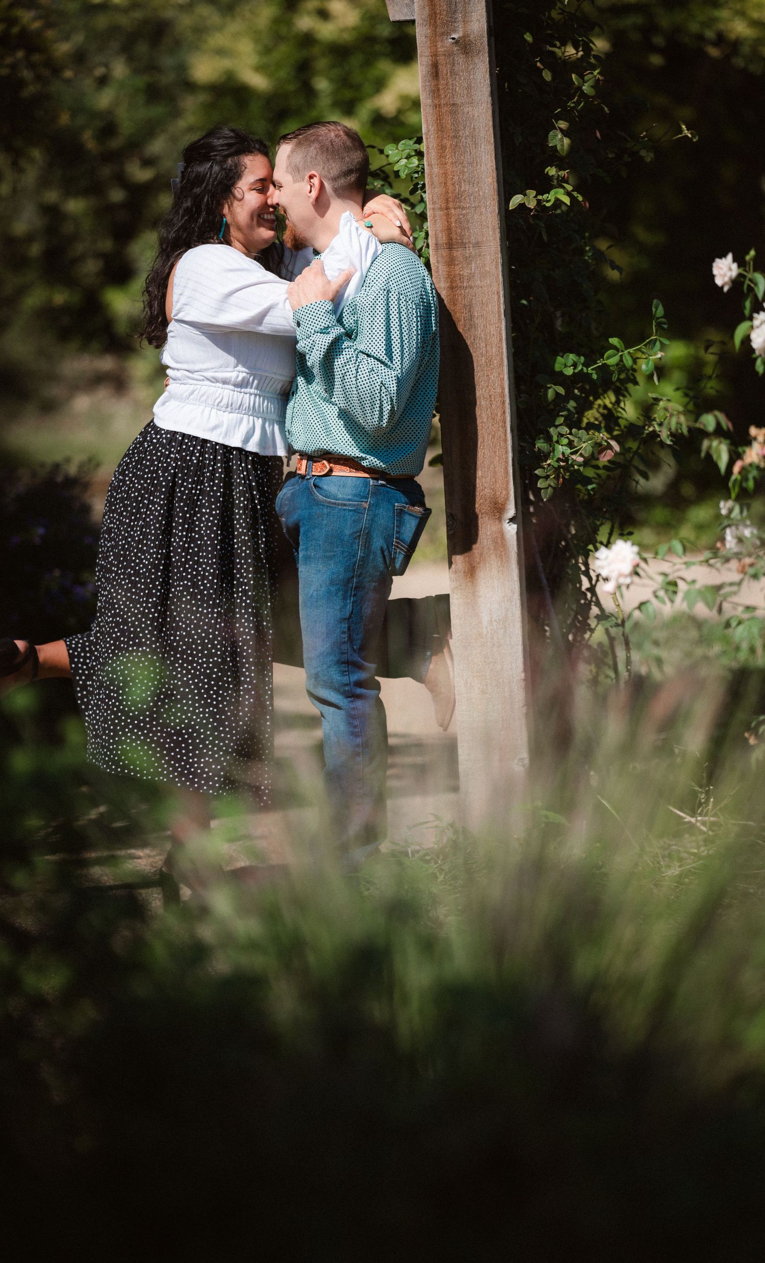 Intimate moment shared between couple near wooden posts in a garden with soft bokeh effect.