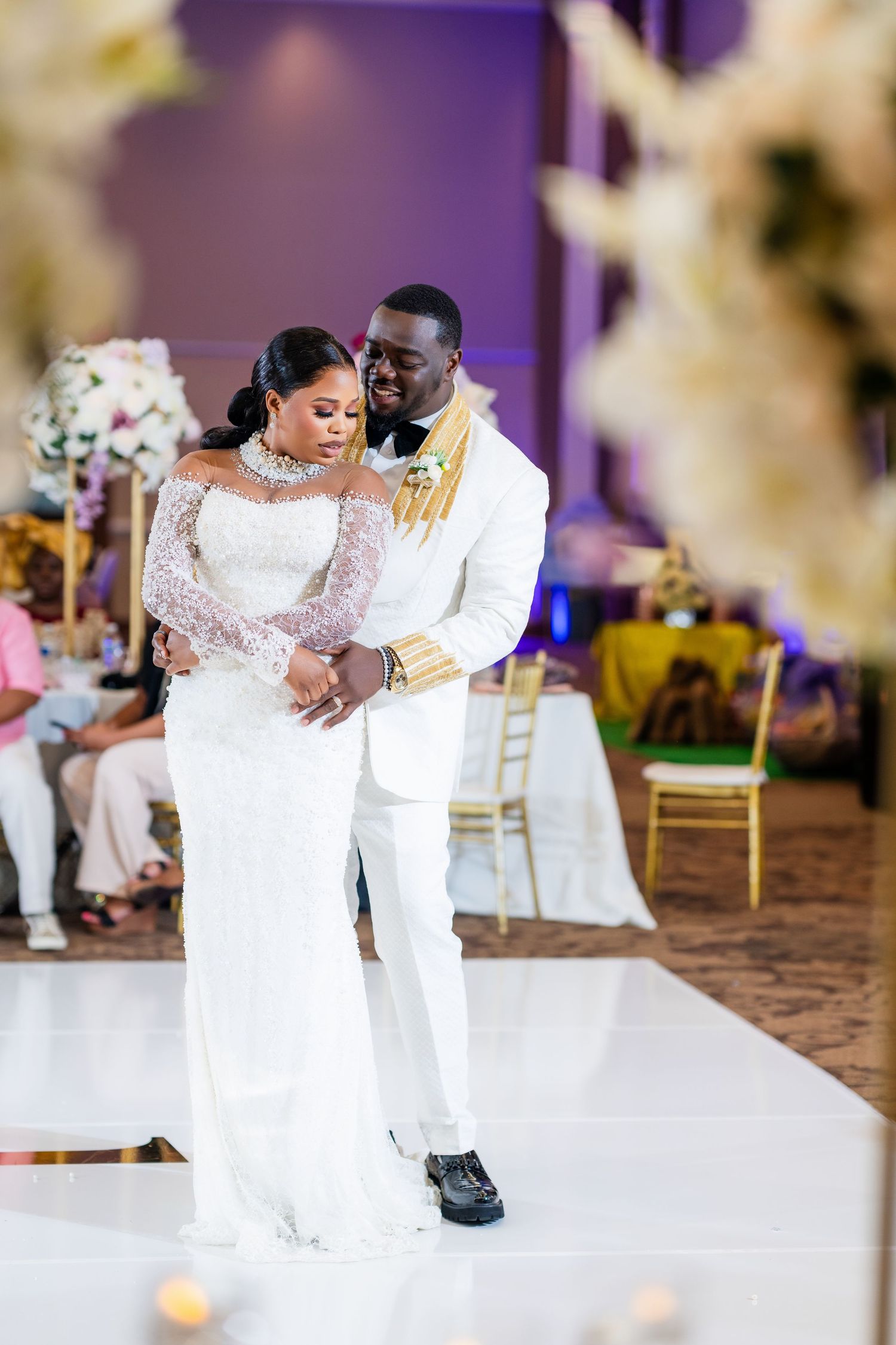 A couple in white attire dancing together on a white dance floor at their wedding reception.