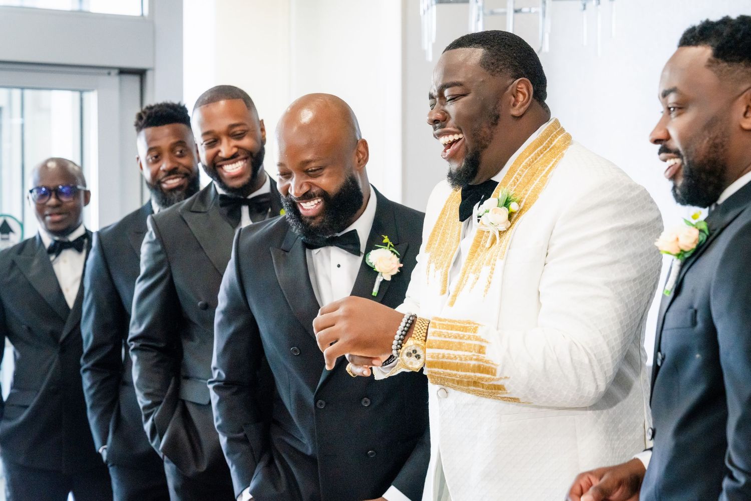 A group of groomsmen in black suits share a lighthearted moment together.