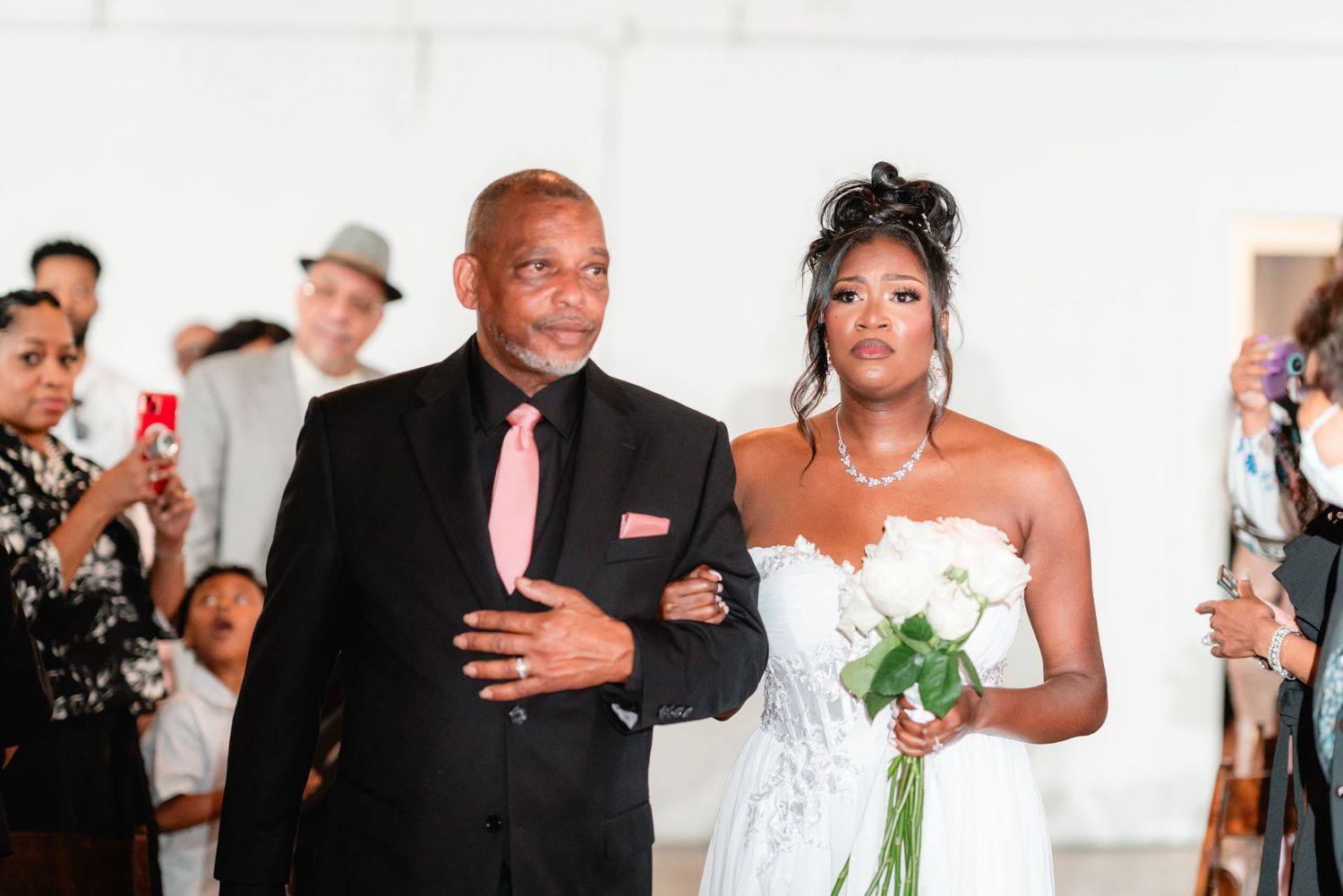 Bride in white gown walking down the aisle during wedding ceremony with escort.
