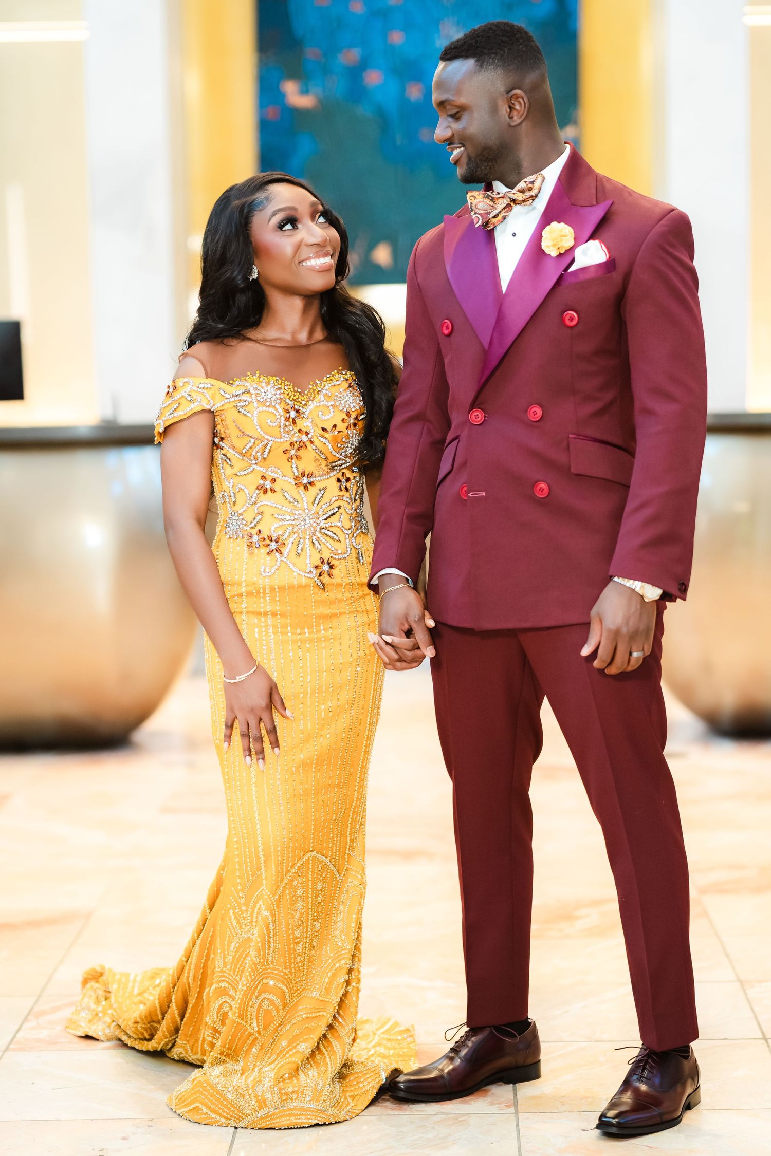 Couple in formal attire posing together, with burgundy suit and yellow beaded dress.