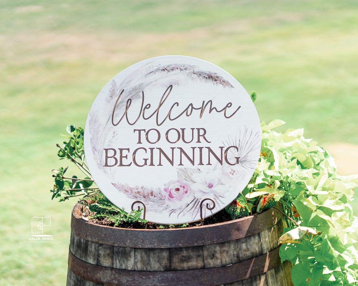 Rustic wedding decor featuring welcome signs on wooden barrels with greenery accents.