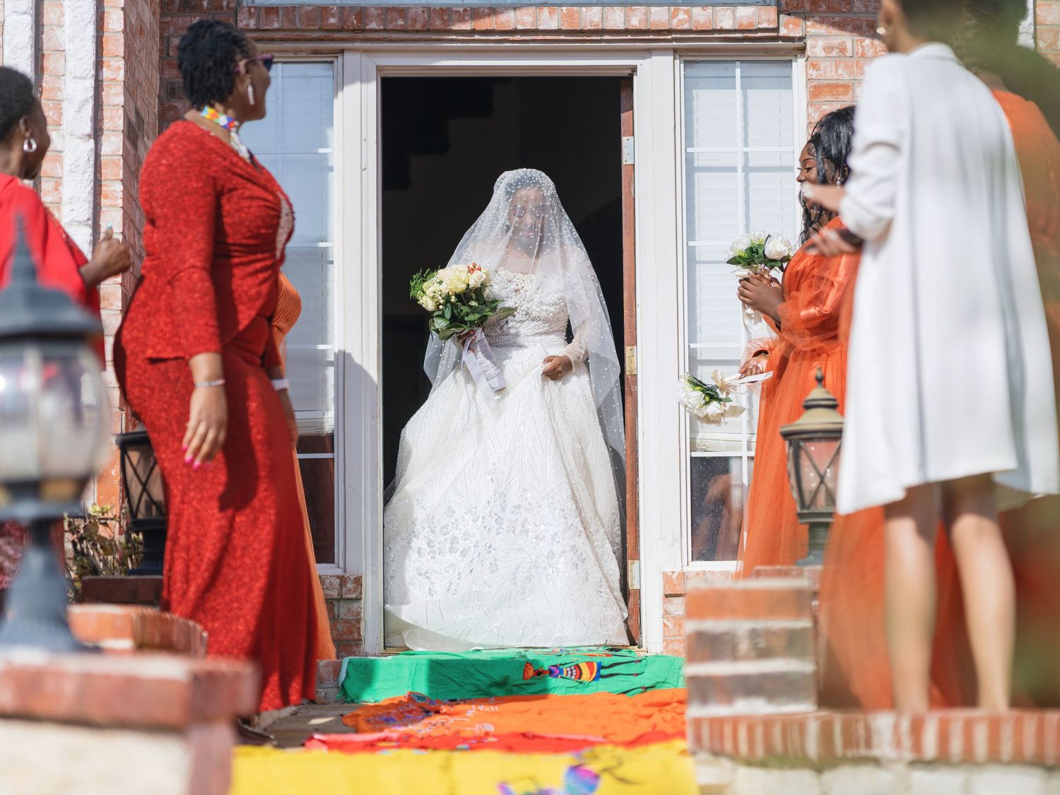 A bride in a white lace gown with veil enters through a doorway decorated with colorful details.