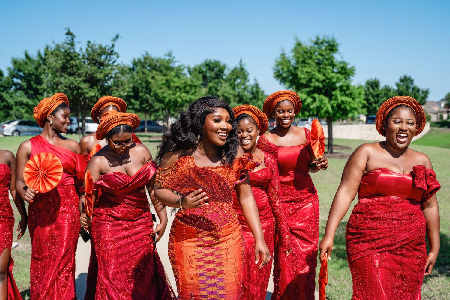 A group wearing coordinated red and orange outfits poses together outdoors on a sunny day.