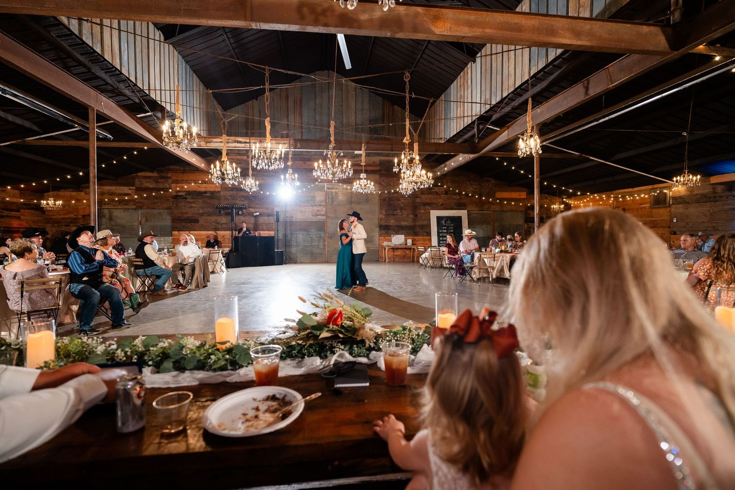 Interior of a rustic barn wedding venue with hanging lights and guest tables.