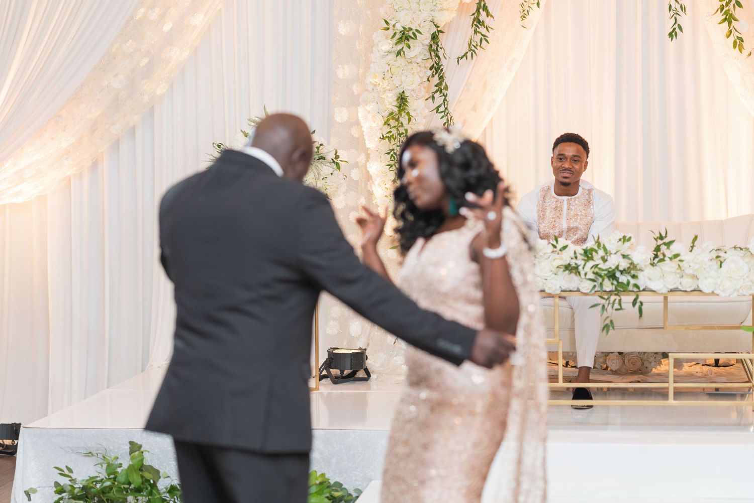 Wedding celebration in elegant white draped venue with hanging floral arrangements.