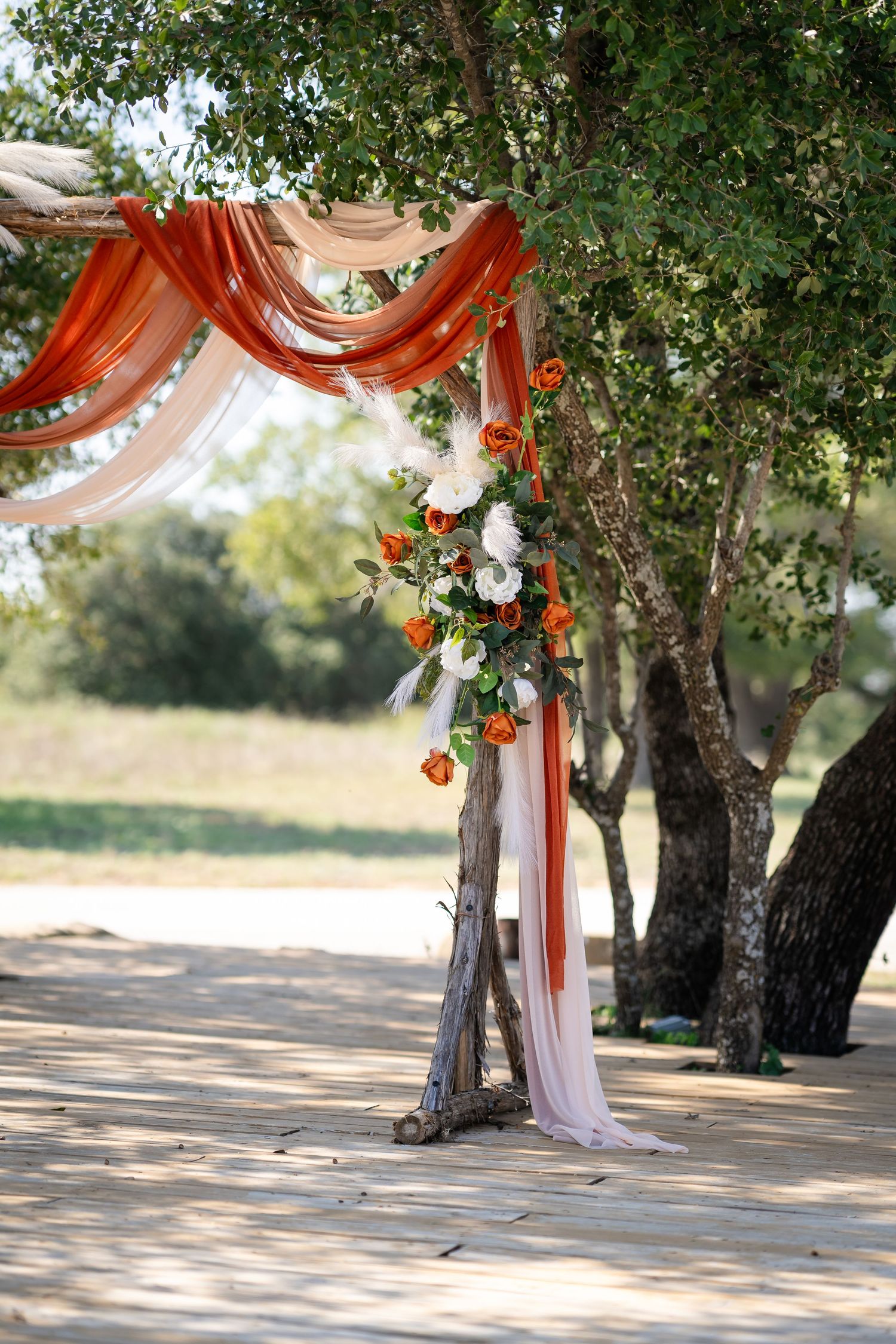 Outdoor wedding arch decorated with red and white fabric and floral arrangements under trees.