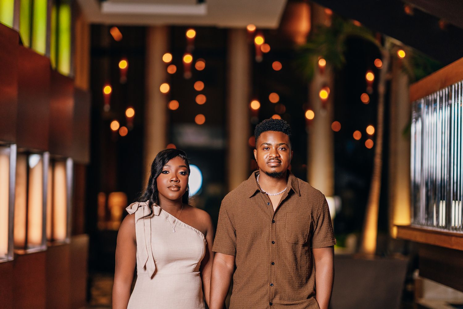 A couple poses together in a venue decorated with warm glowing string lights creating a romantic atmosphere.
