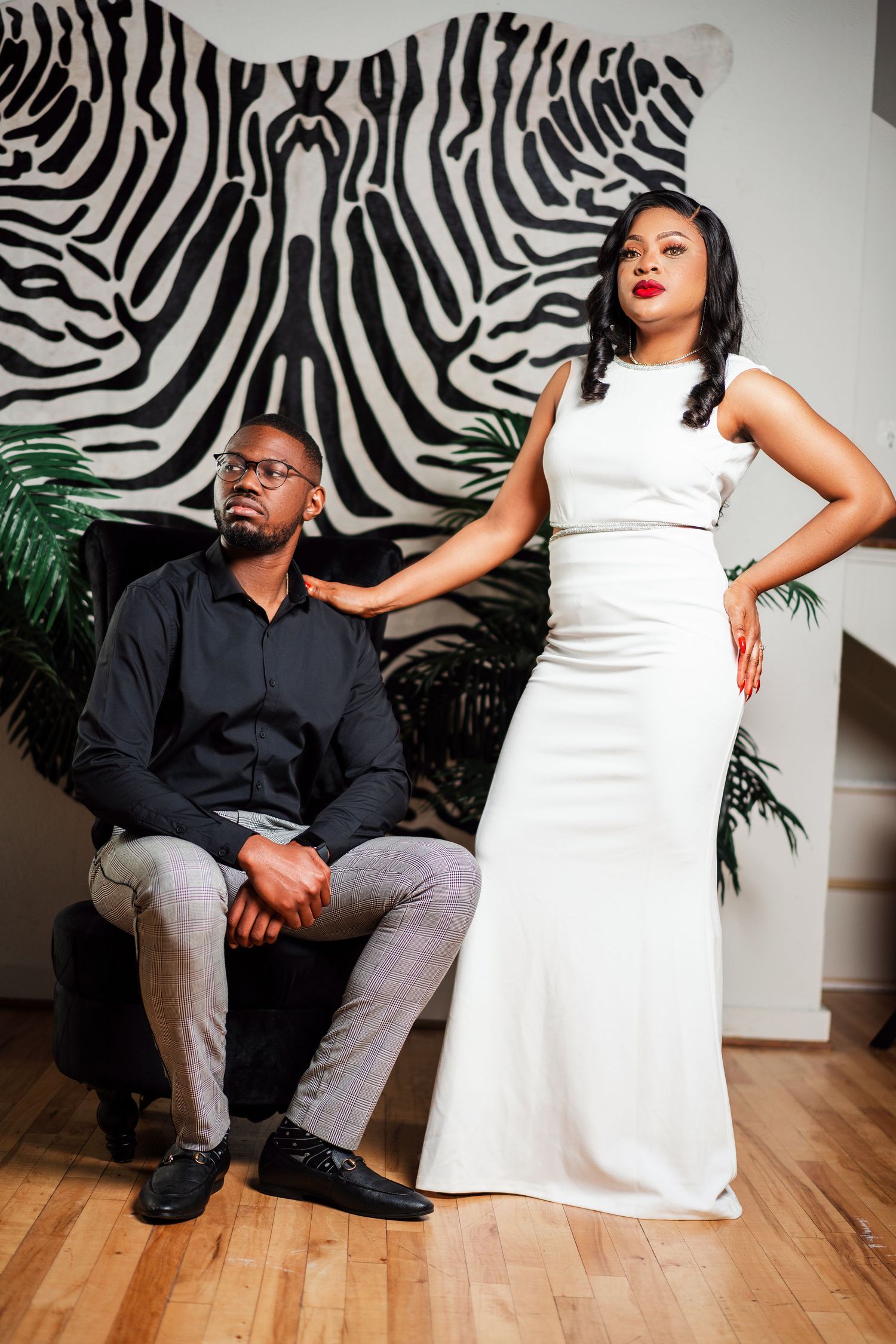 Stylish couple poses against zebra print wall in modern studio setting with dramatic lighting and hardwood floors.