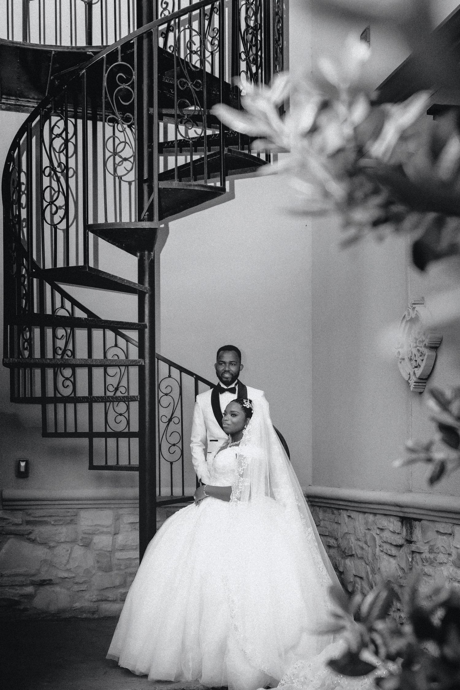 A black and white wedding photo featuring an elegant spiral staircase and a bride in a full tulle ballgown.