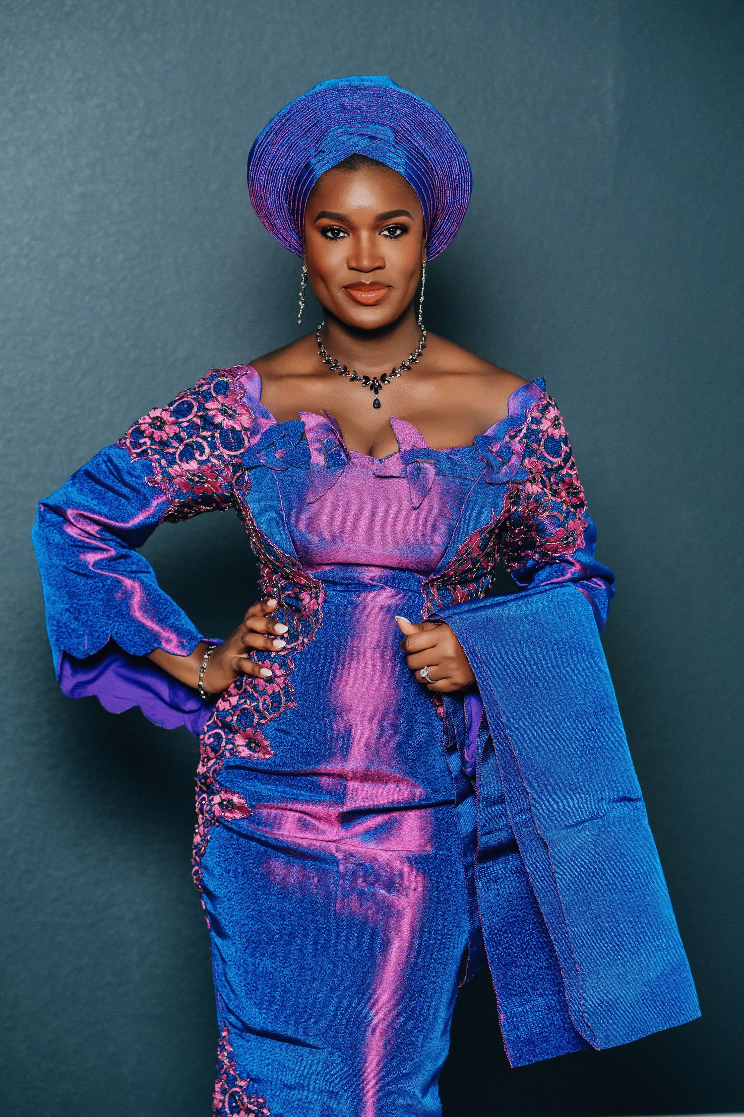 Full length shot of blue and purple traditional African formal wear with matching gele and accessories.