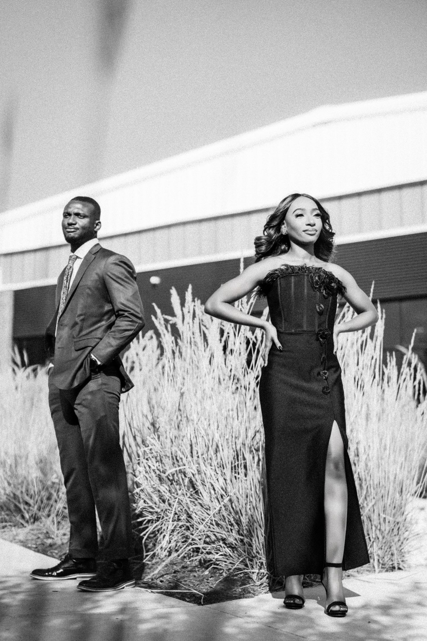 Black and white photo of elegantly dressed couple posing dramatically by ornamental grasses.