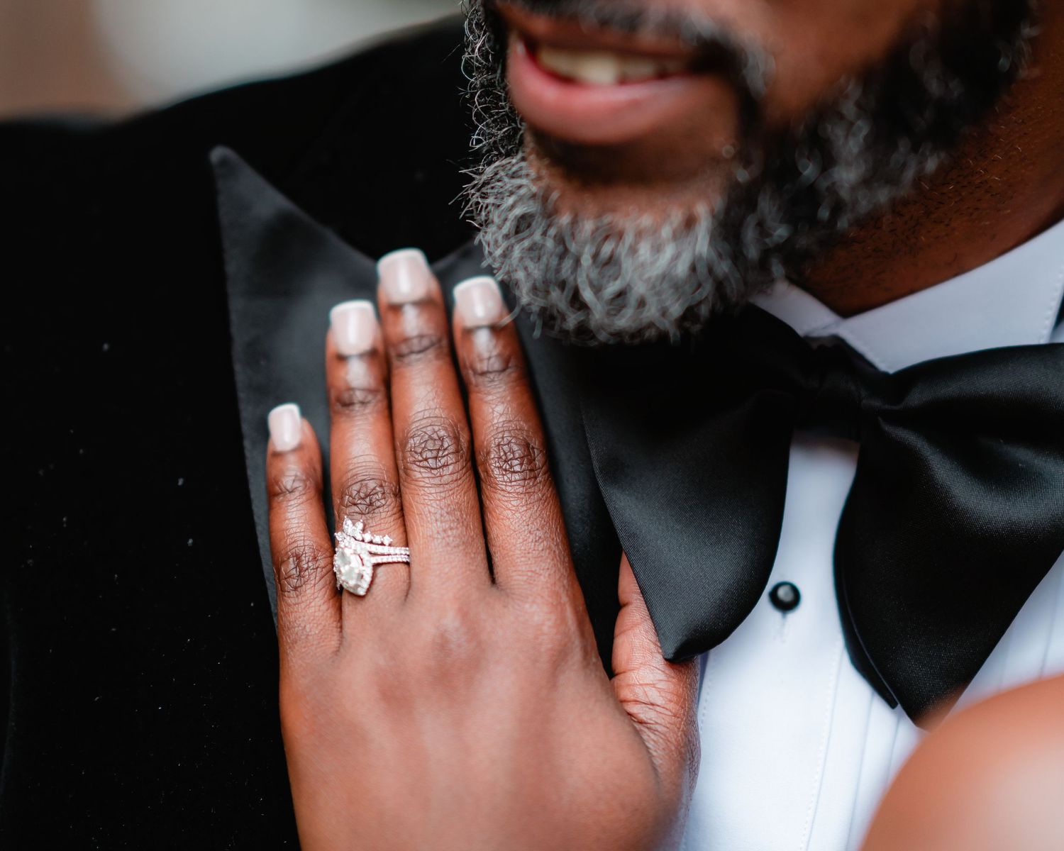 Close-up details of wedding rings and hands against formal black and white attire.