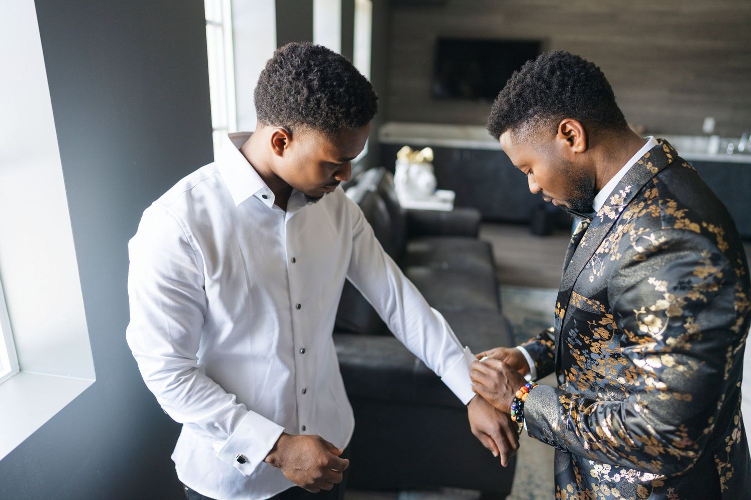 Two people in a modern space looking down at their hands, one wearing a white shirt and one in a camouflage jacket.
