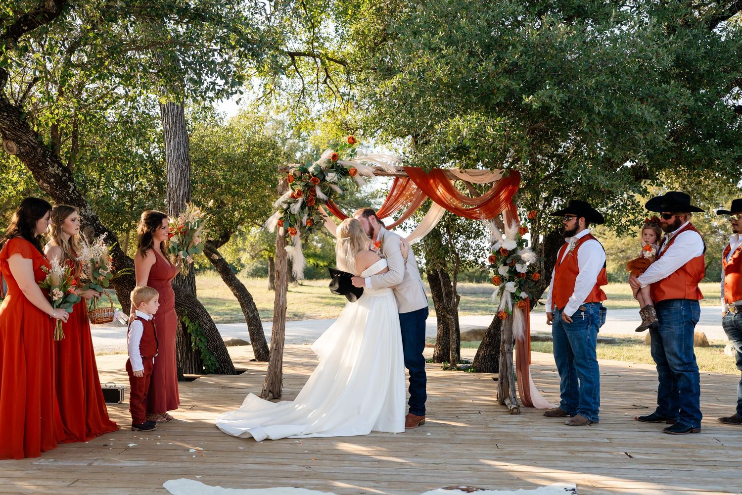 Wedding guests in red dresses celebrate outdoors under trees during a ceremony.