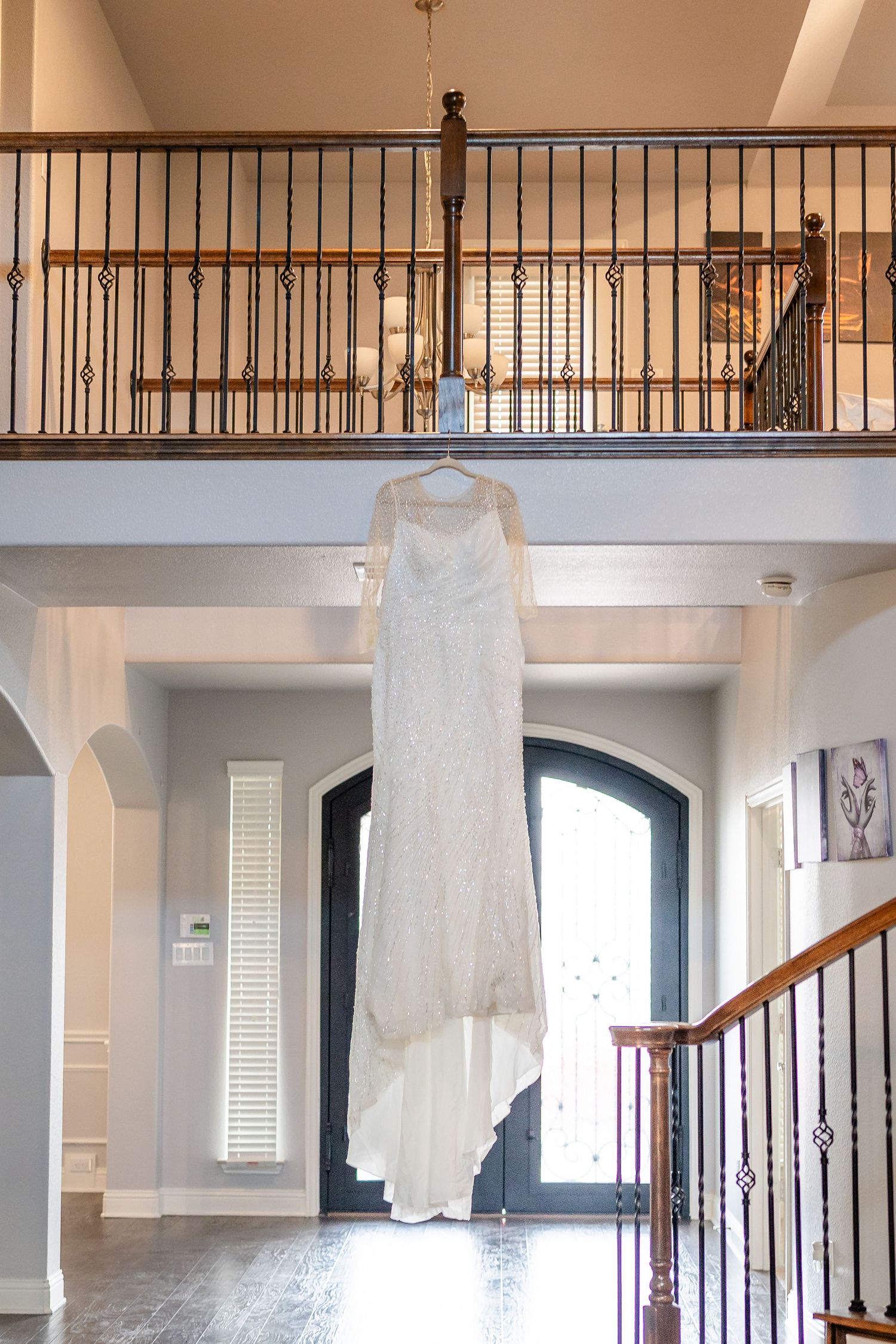 White wedding dress hangs elegantly in a modern interior with wrought iron stair railings.