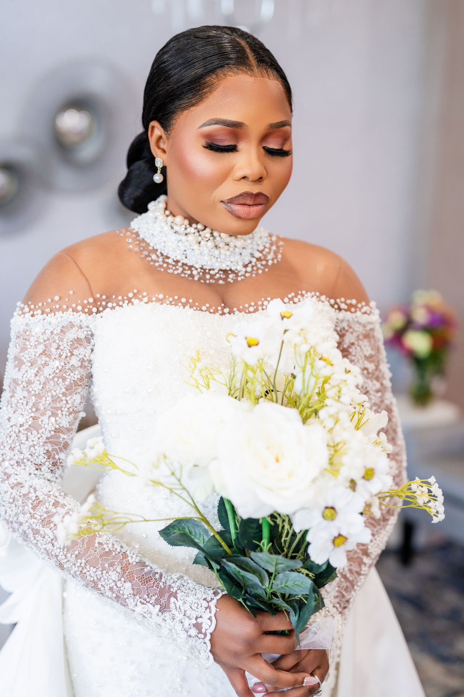 A stunning bridal portrait featuring an elegant white lace gown with a crystal neckline and a bouquet of white flowers.