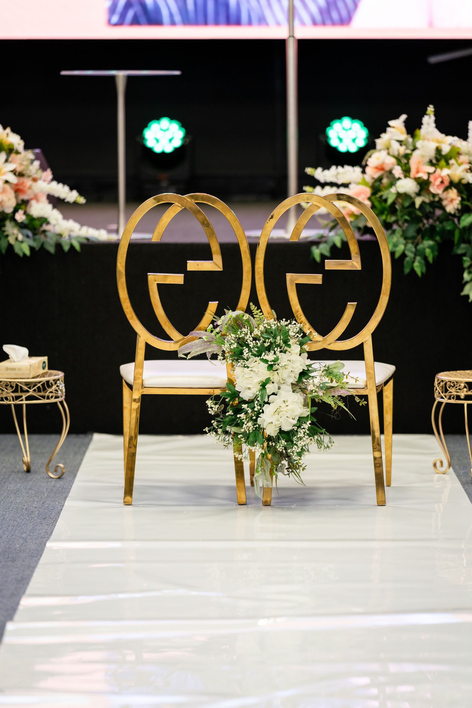 Elegant gold chairs and floral arrangements line a modern wedding ceremony space.