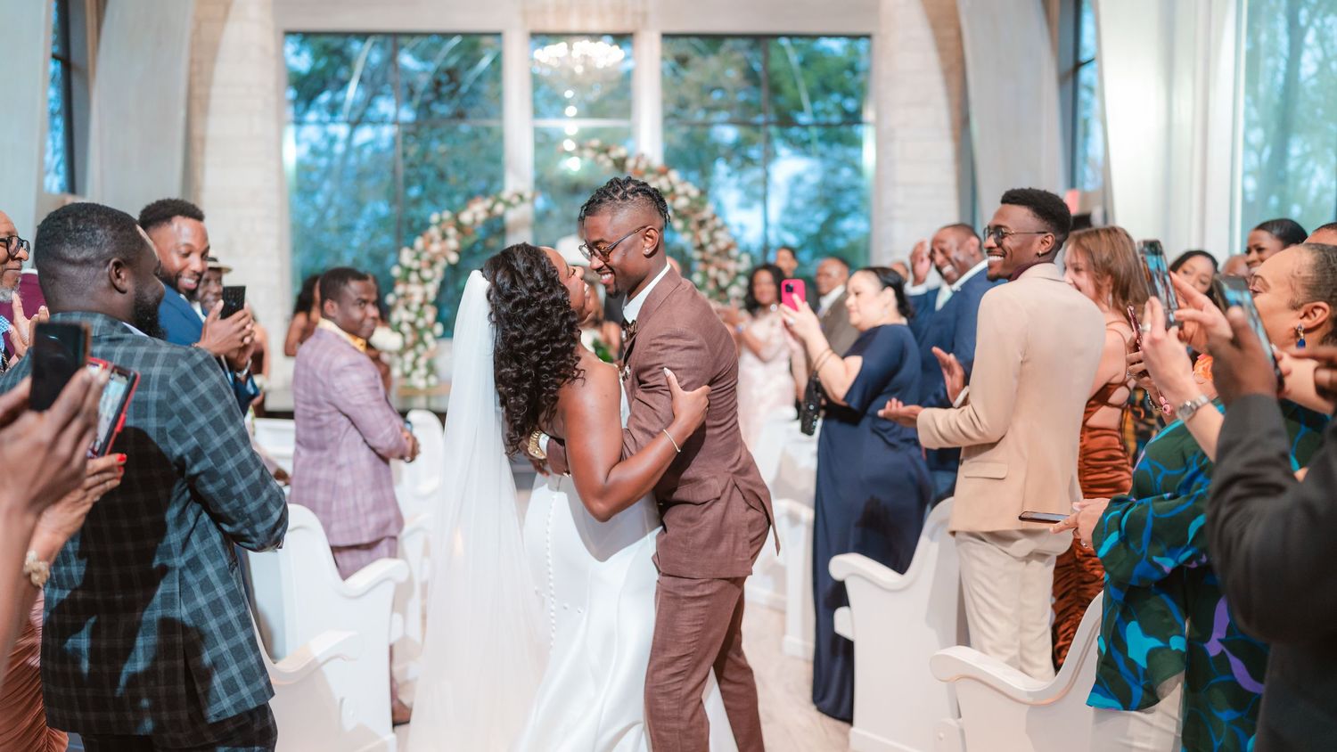 Wedding celebration with guests cheering during ceremony in bright, airy chapel.