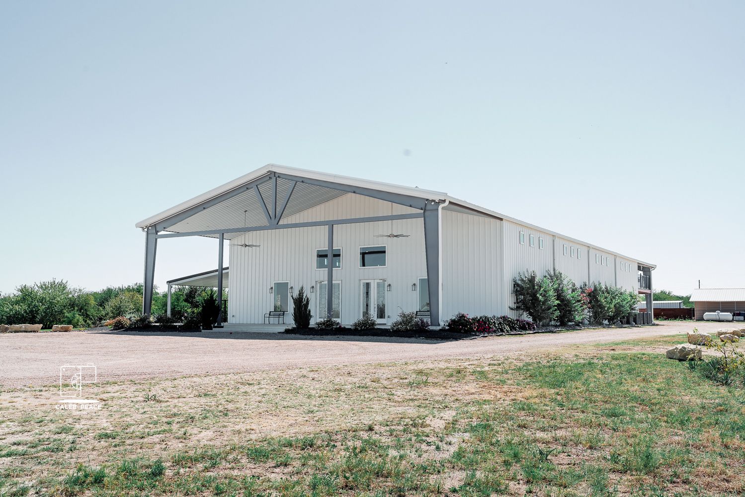White metal storage buildings and barns sit on flat terrain under a blue sky with sparse vegetation in the foreground.