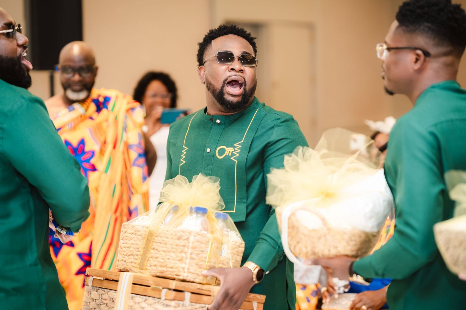 Wedding reception scene with guests in green attire and decorative gift baskets.