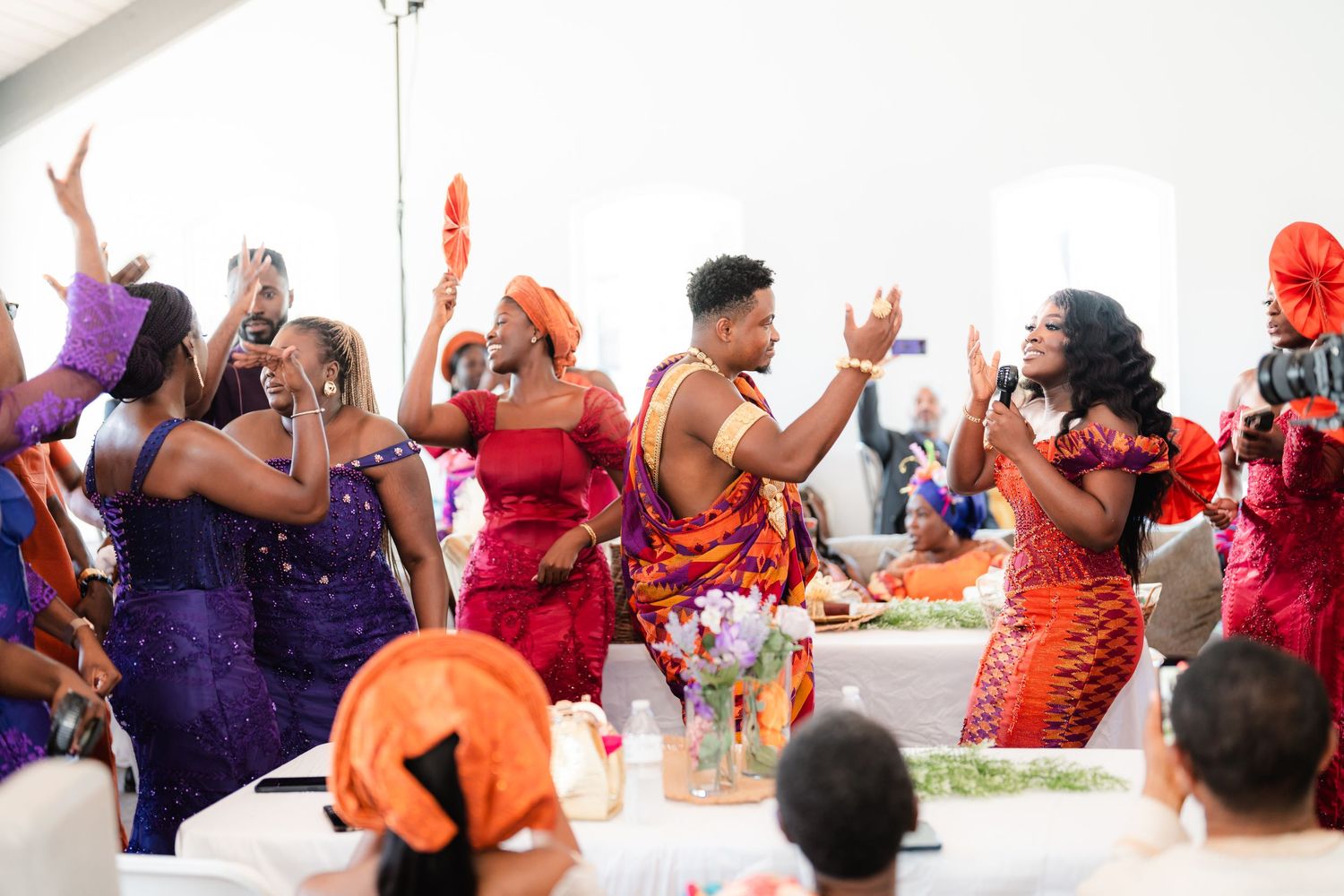 Wedding celebration scene with people dancing and celebrating in orange and purple attire.
