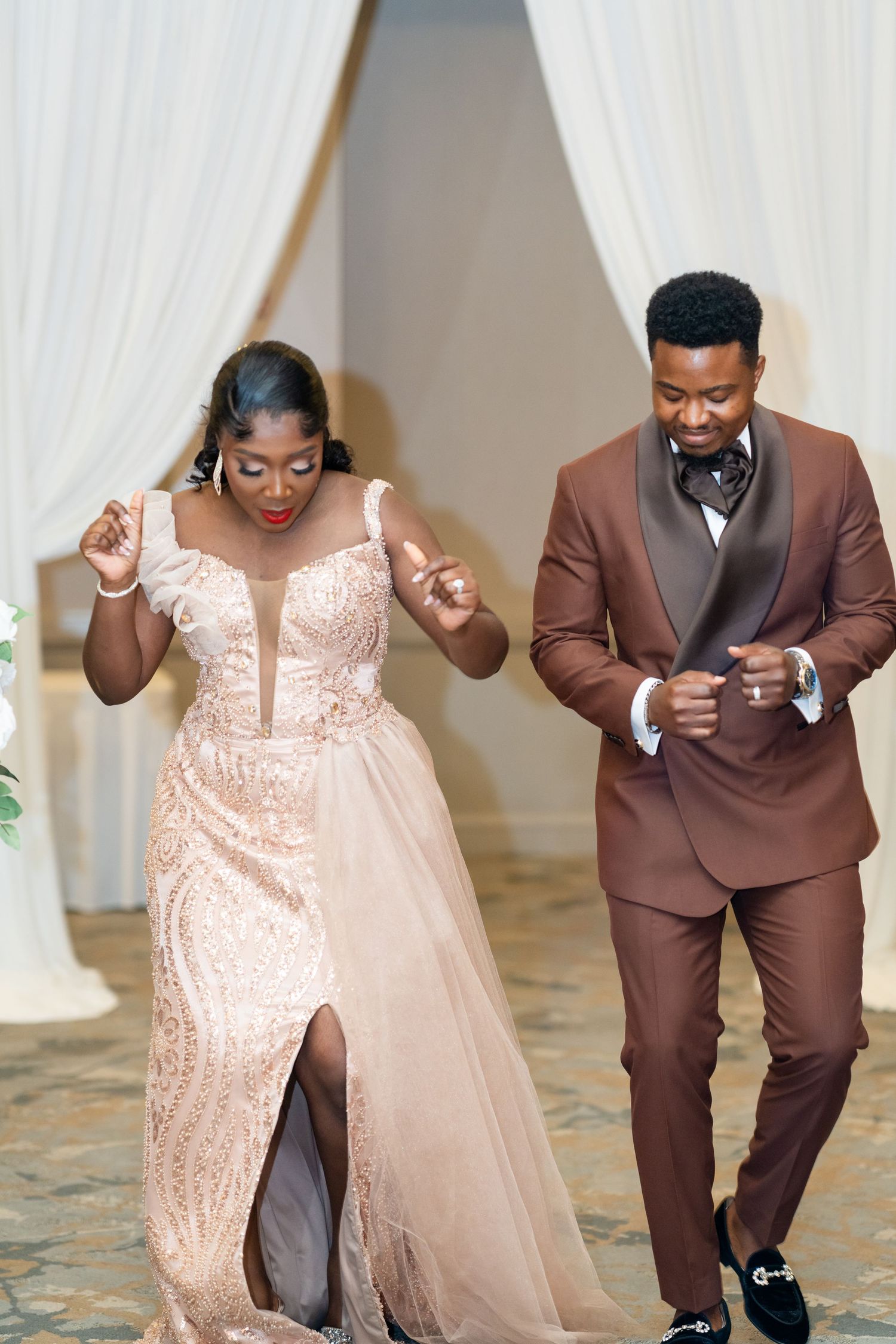Wedding couple performs joyful dance moves in brown suit and blush sequin dress.