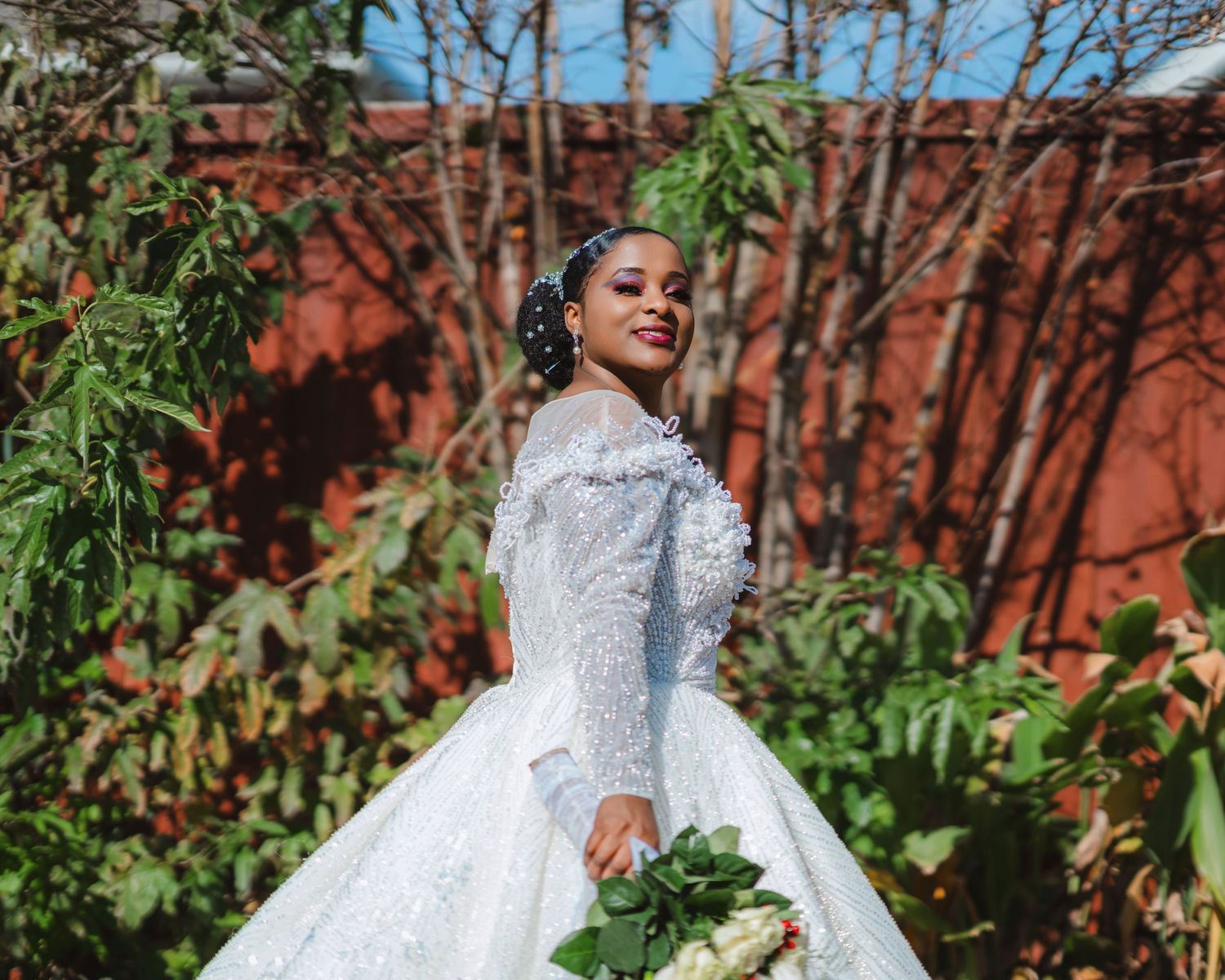 A stunning bridal portrait featuring an ornate white lace ball gown against a red brick wall.