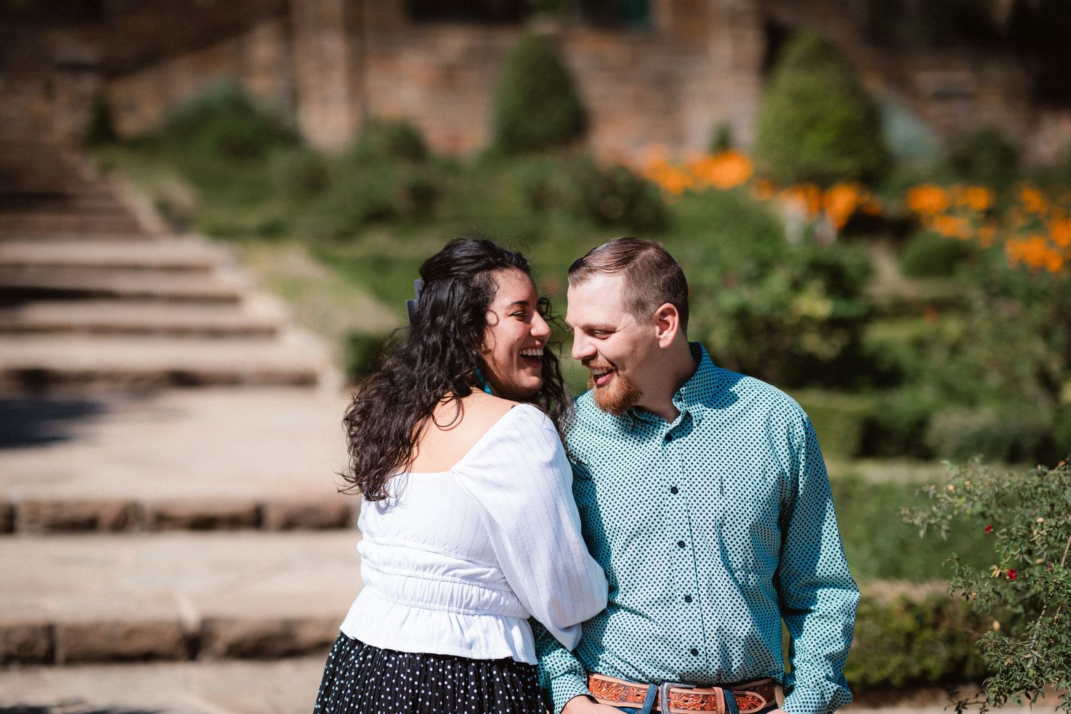 A couple shares an intimate moment in a lush garden setting with vibrant orange flowers in the background.