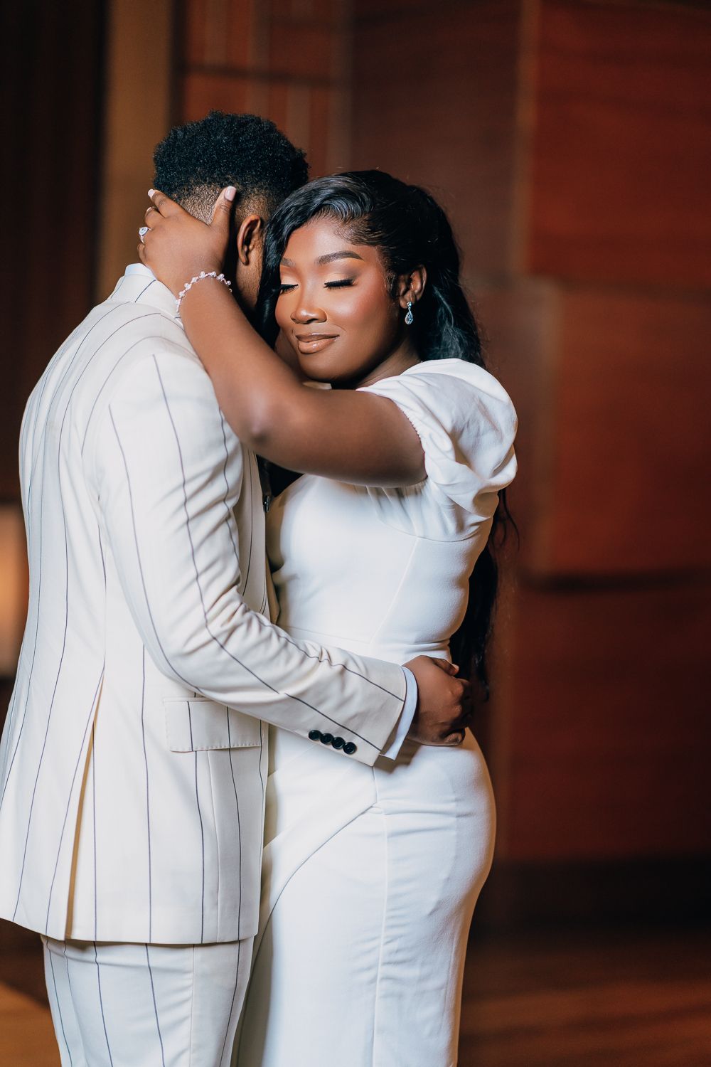 Intimate indoor portrait of a couple embracing in elegant white attire.