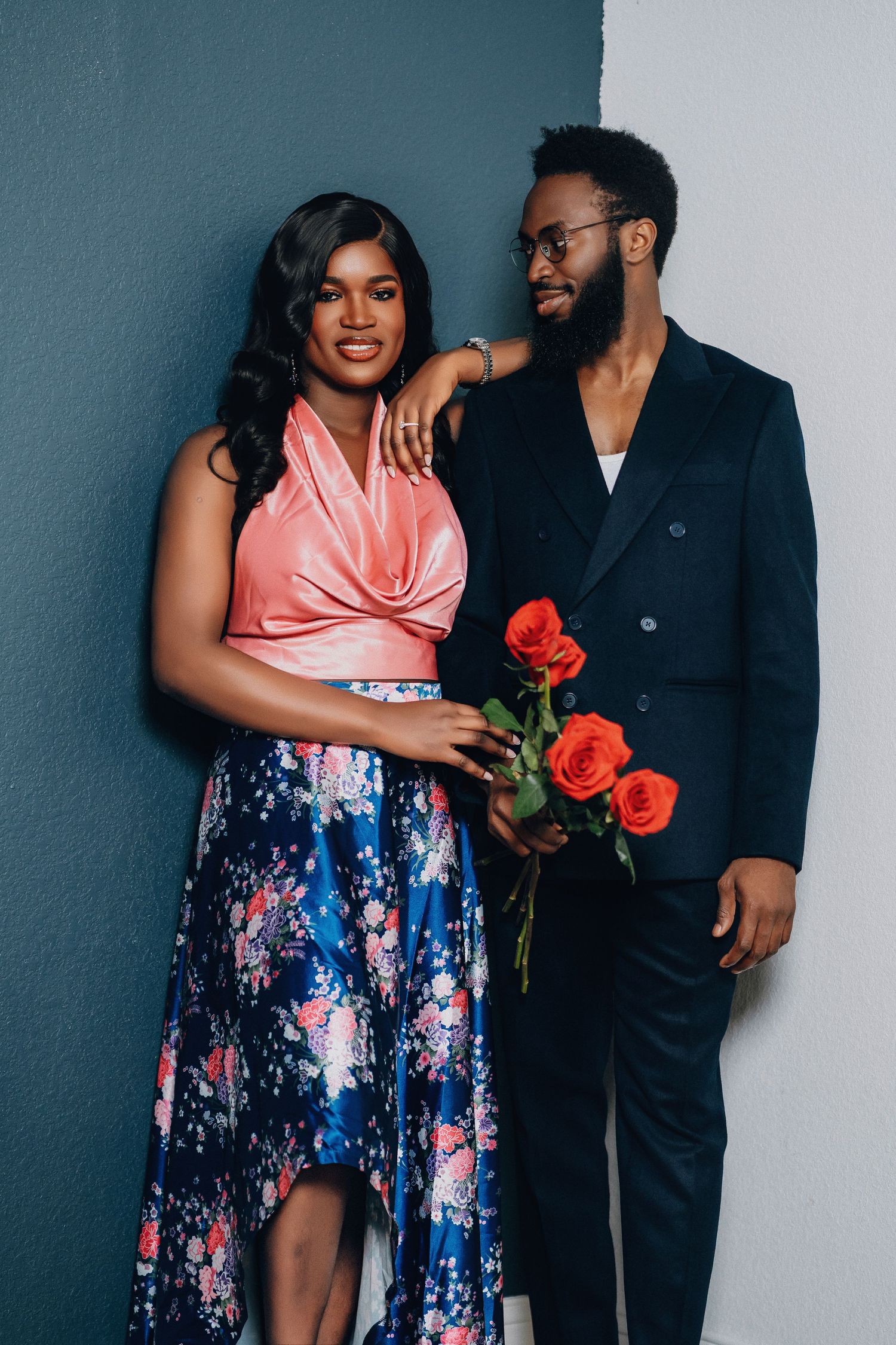 A romantic photoshoot featuring a couple in formal wear sharing tender moments against a gray wall.