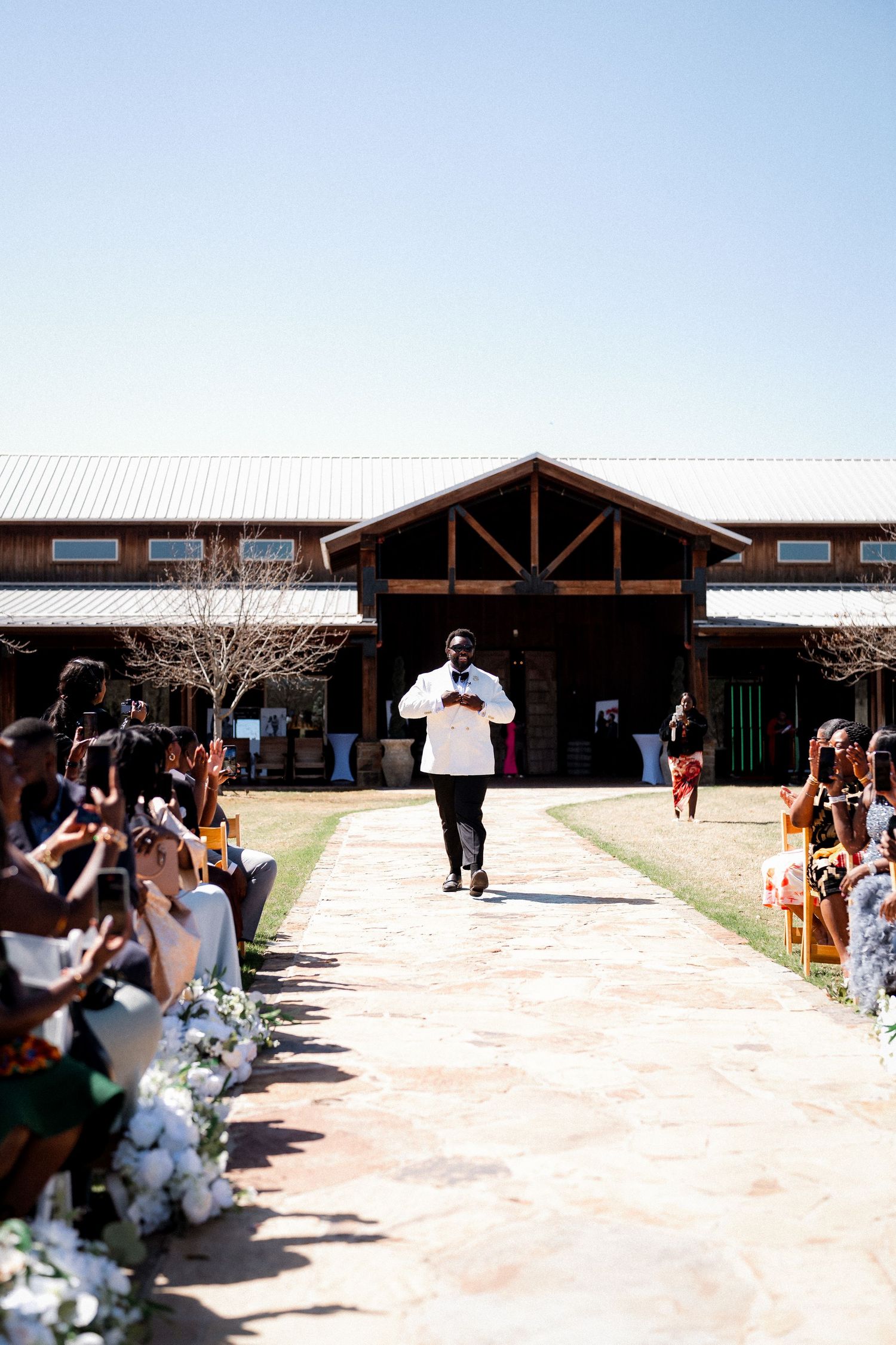 A person walks down an outdoor wedding aisle lined with guests and floral decorations.
