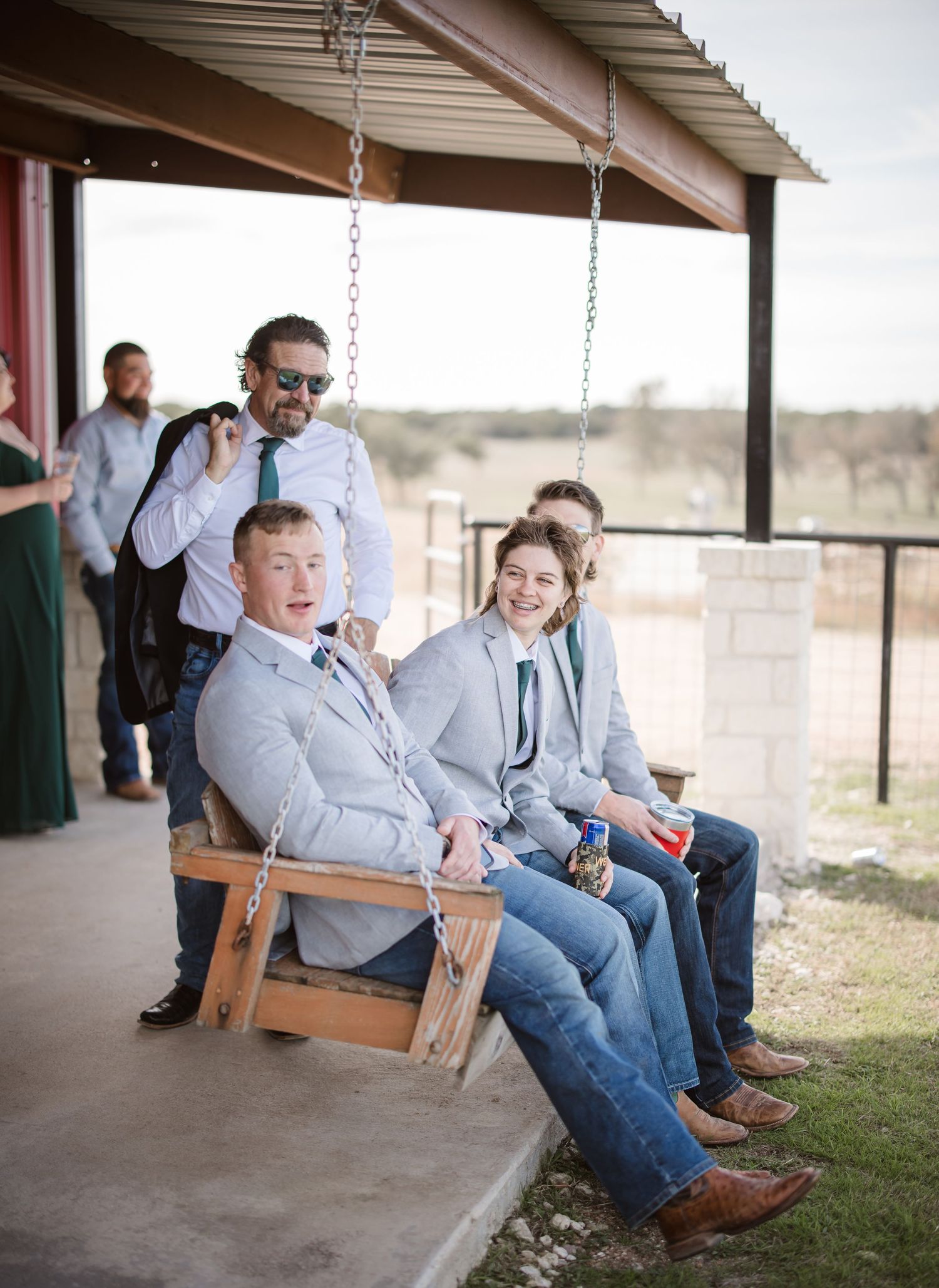 Group relaxing on wooden porch swings at rustic venue.