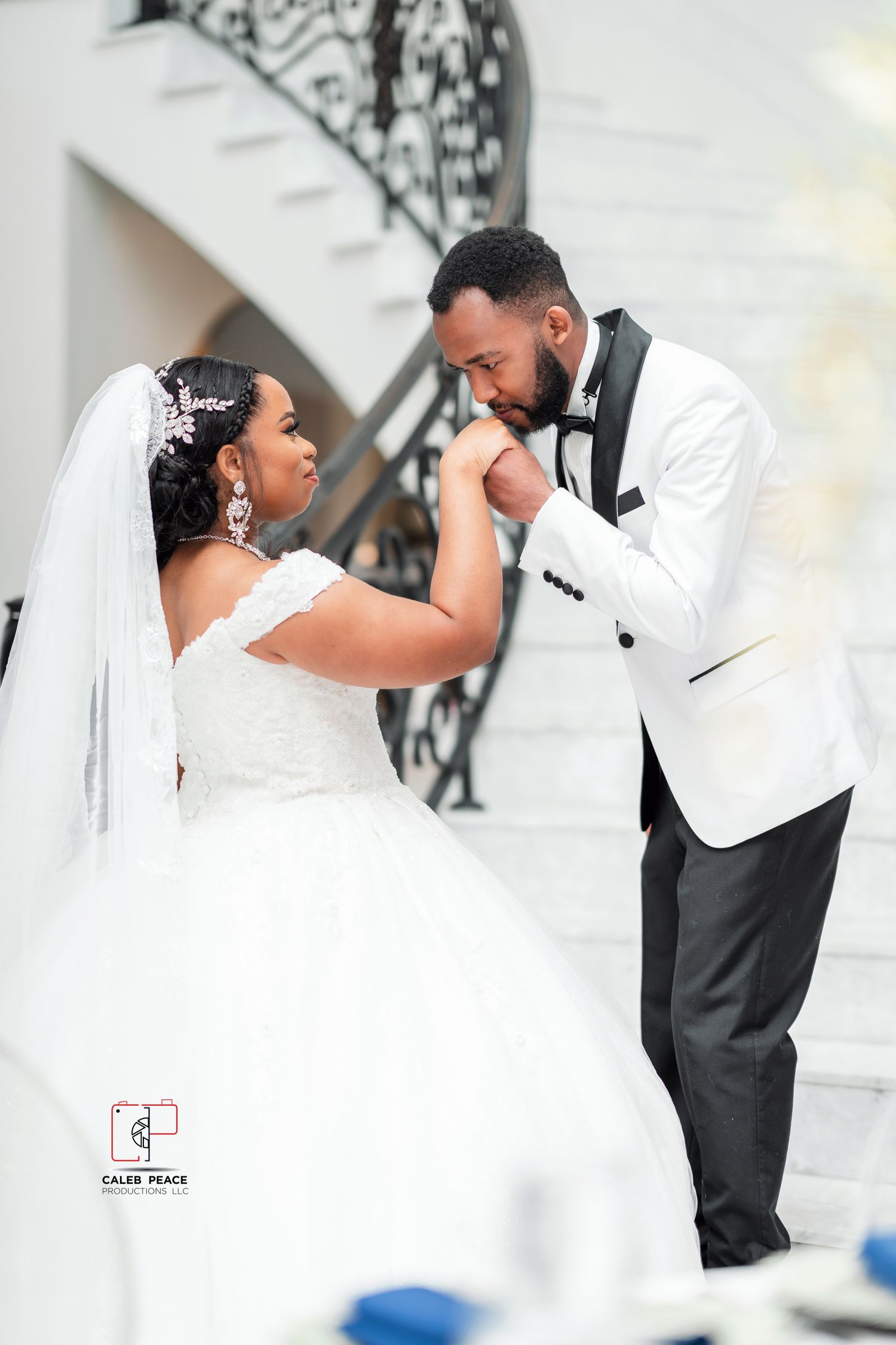 A romantic wedding couple shares an intimate moment in formal attire against an elegant white backdrop.