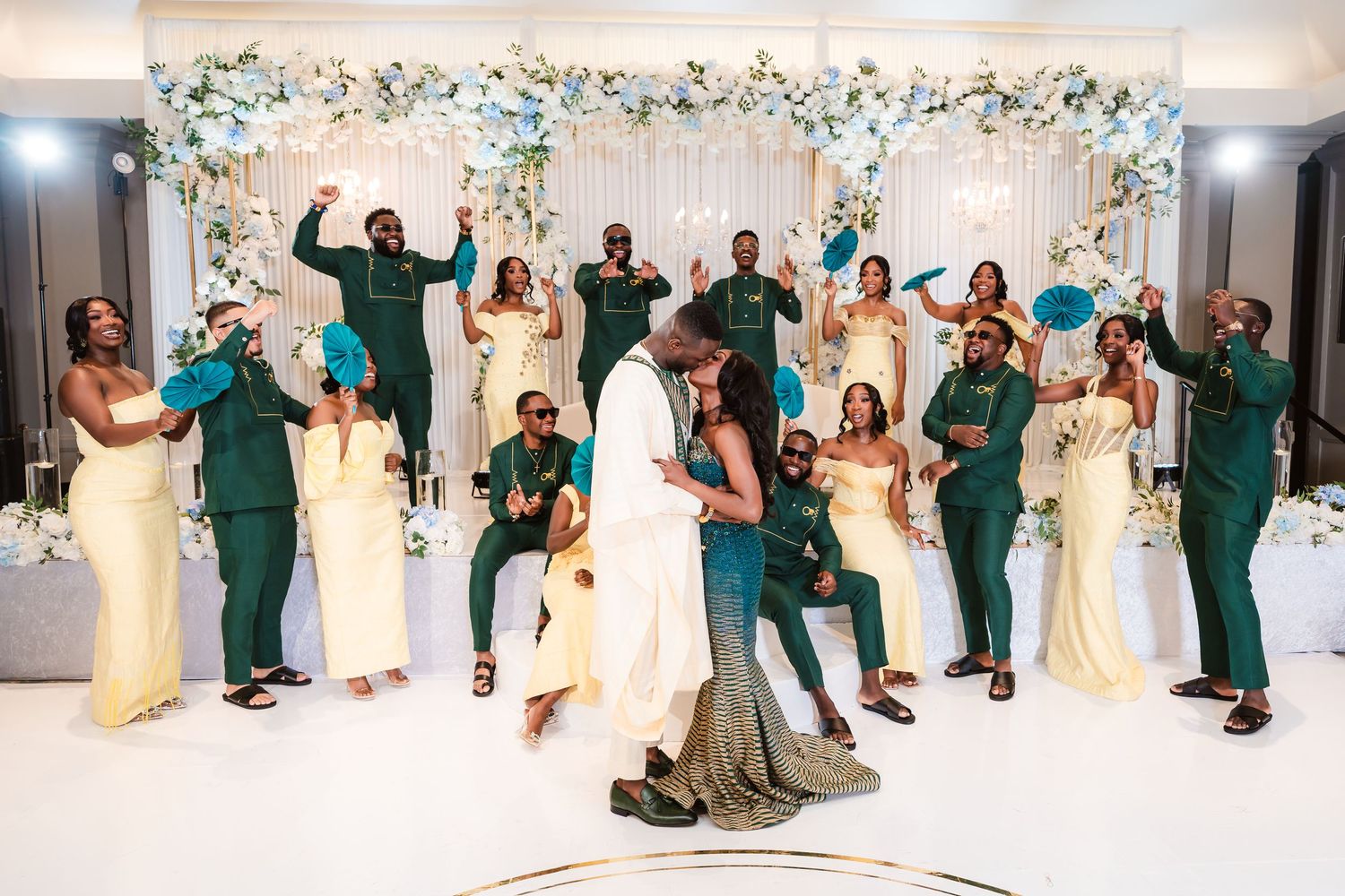 Wedding celebration with green and gold attire in front of a floral arch backdrop.