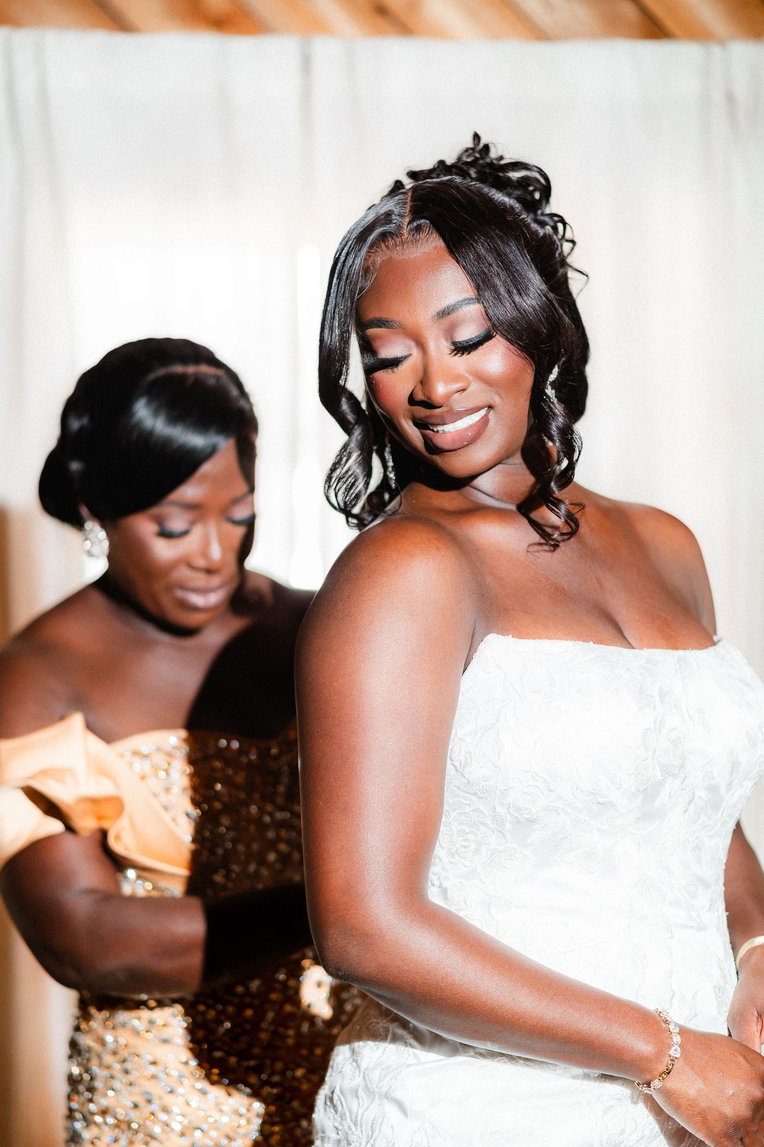 A close-up shot shows two people during a wedding preparation moment in elegant dresses.