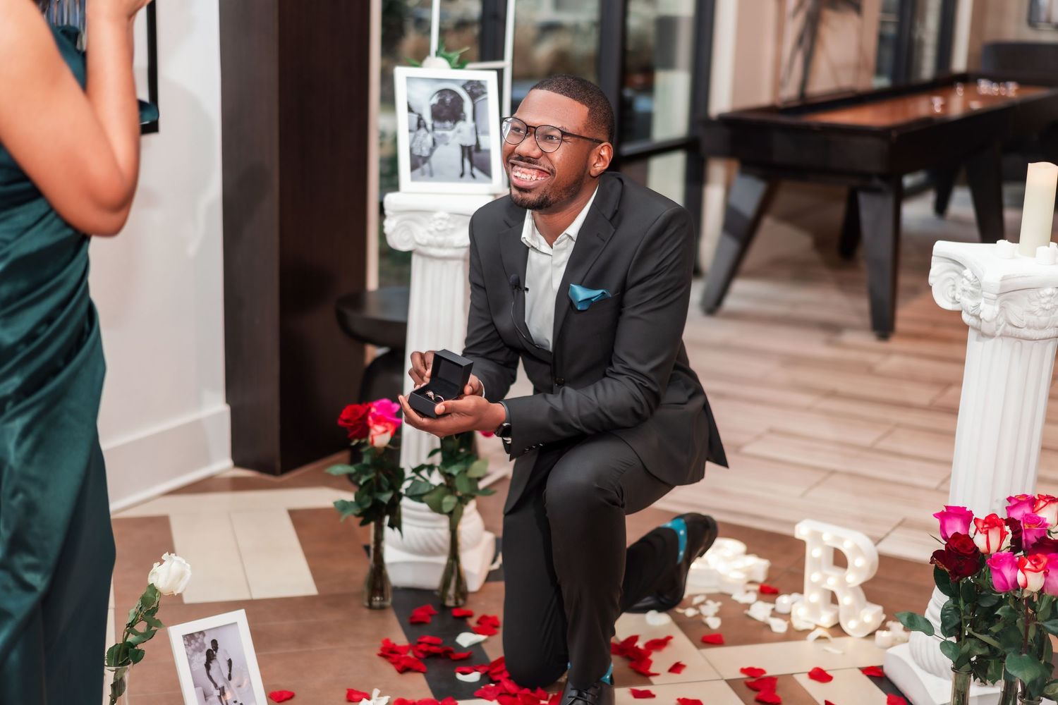 A romantic proposal moment on stairs with bright pink roses and white petals scattered around.