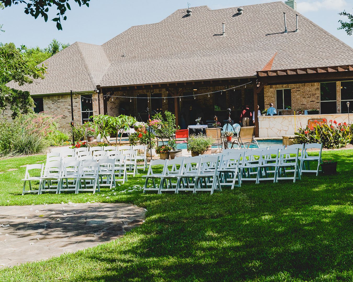 Outdoor wedding ceremony setup with white chairs on a lawn in front of a stone house.
