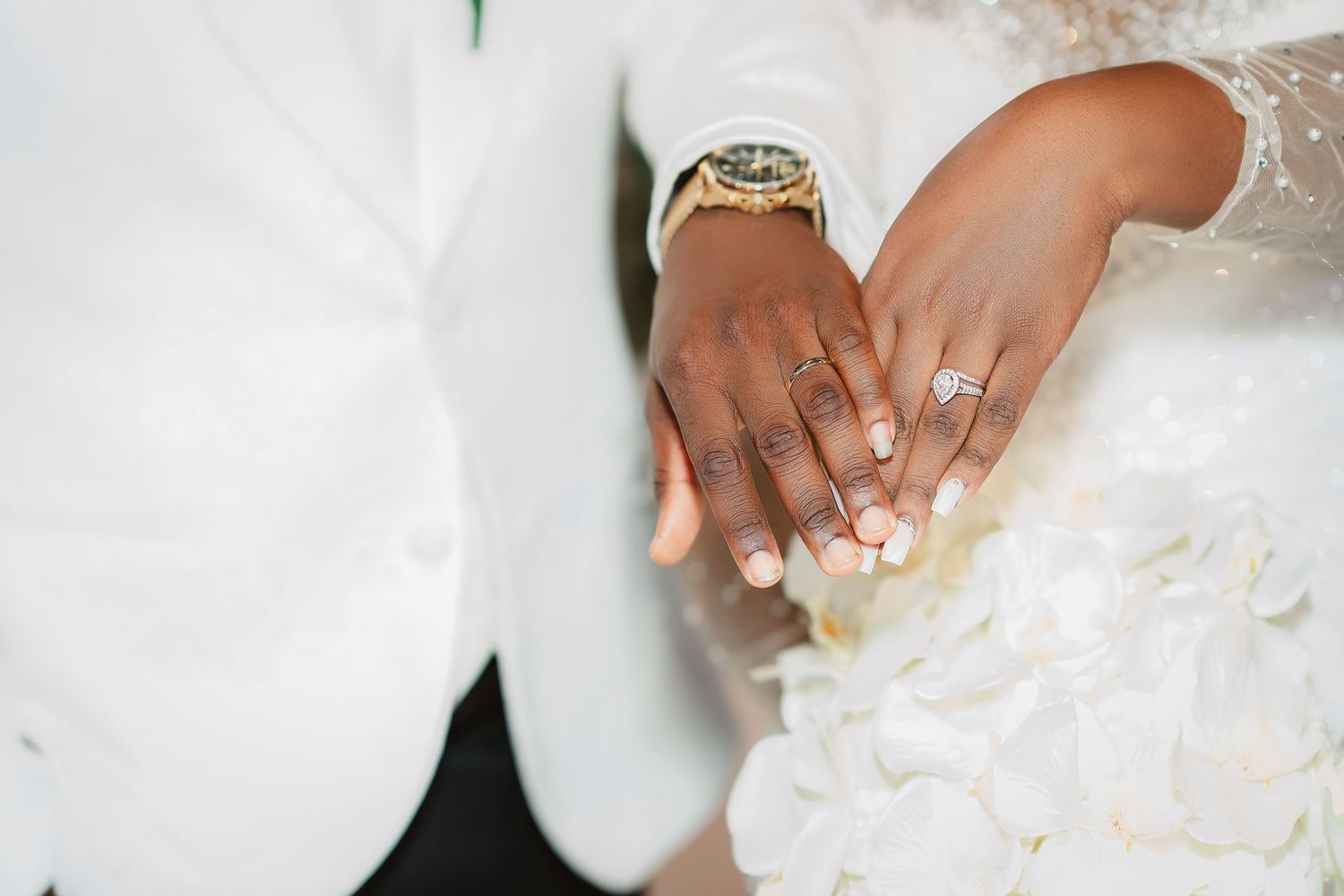 Wedding hands with rings and white floral bouquet showing during a ceremony.