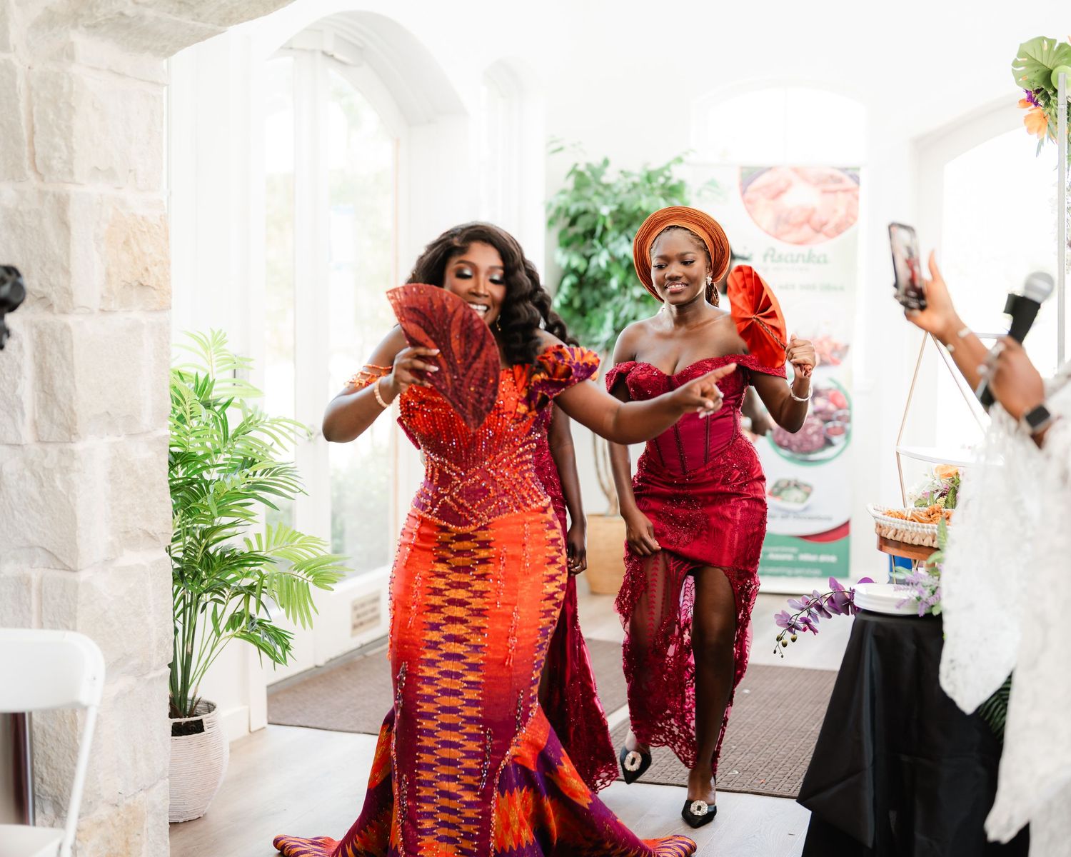 Joyful wedding reception scene with guests in red attire dancing and celebrating in bright indoor venue.