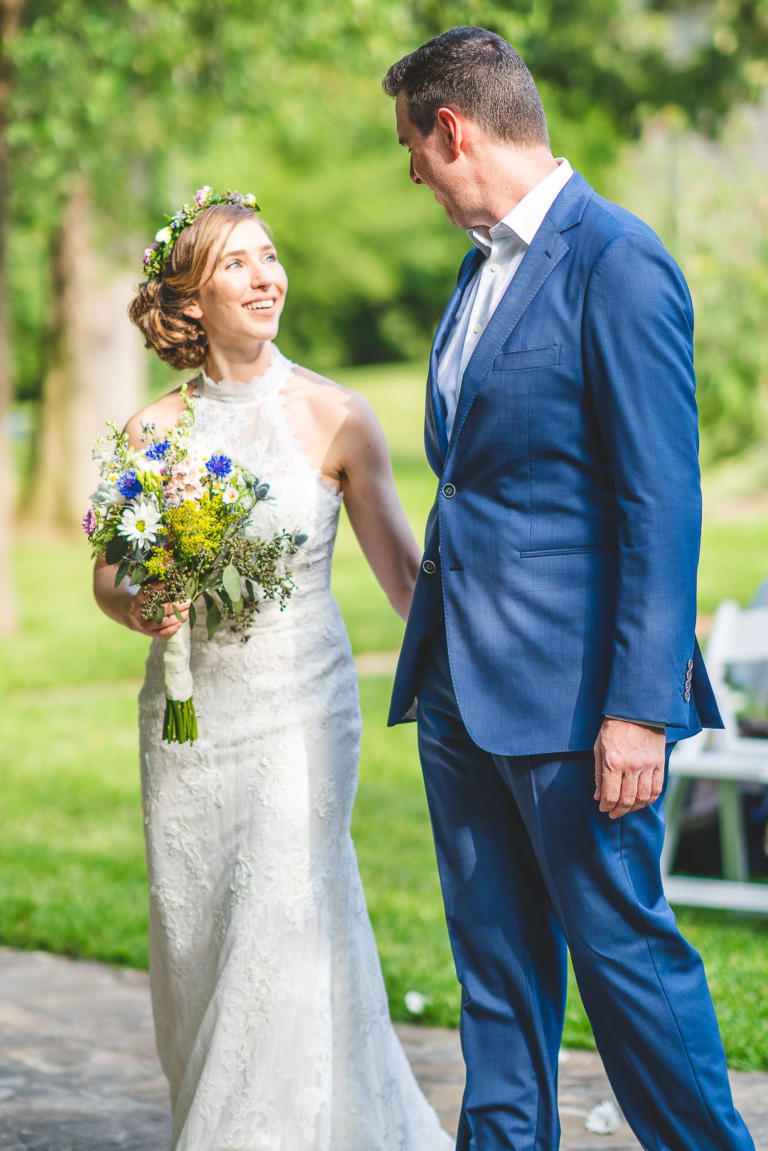 A couple shares a joyful moment outdoors in wedding attire with the bride in white lace and groom in navy blue suit.