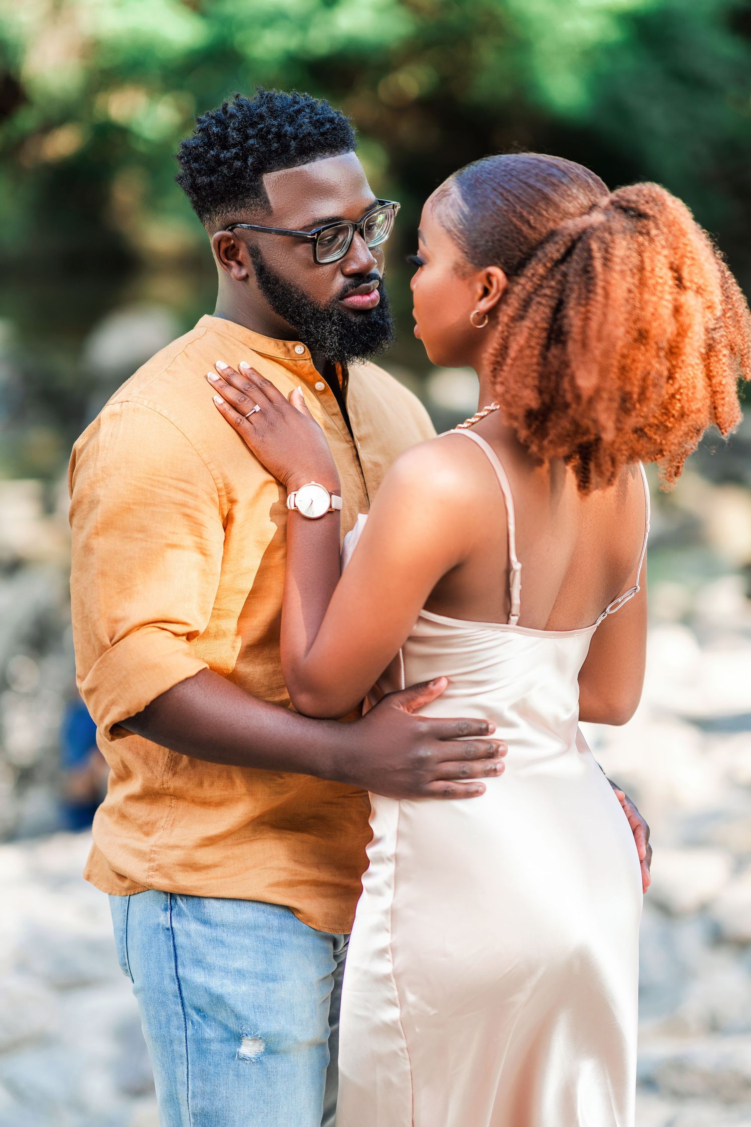 A romantic couple shares an intimate moment outdoors, with one wearing an orange shirt and light jeans.