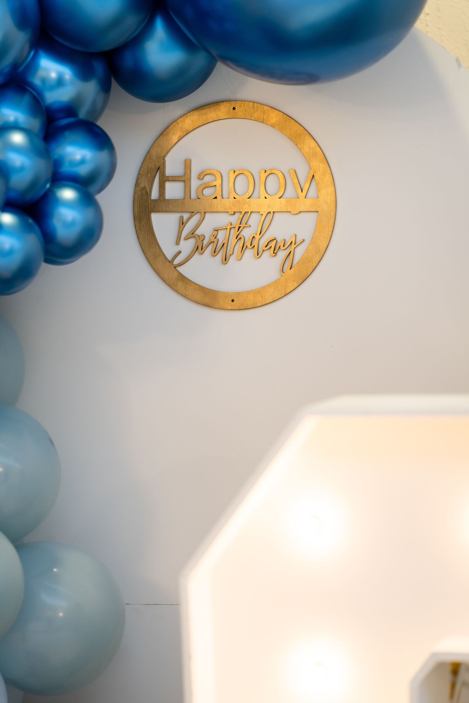 Metallic blue balloon arch with gold birthday text decorations against a white wall.