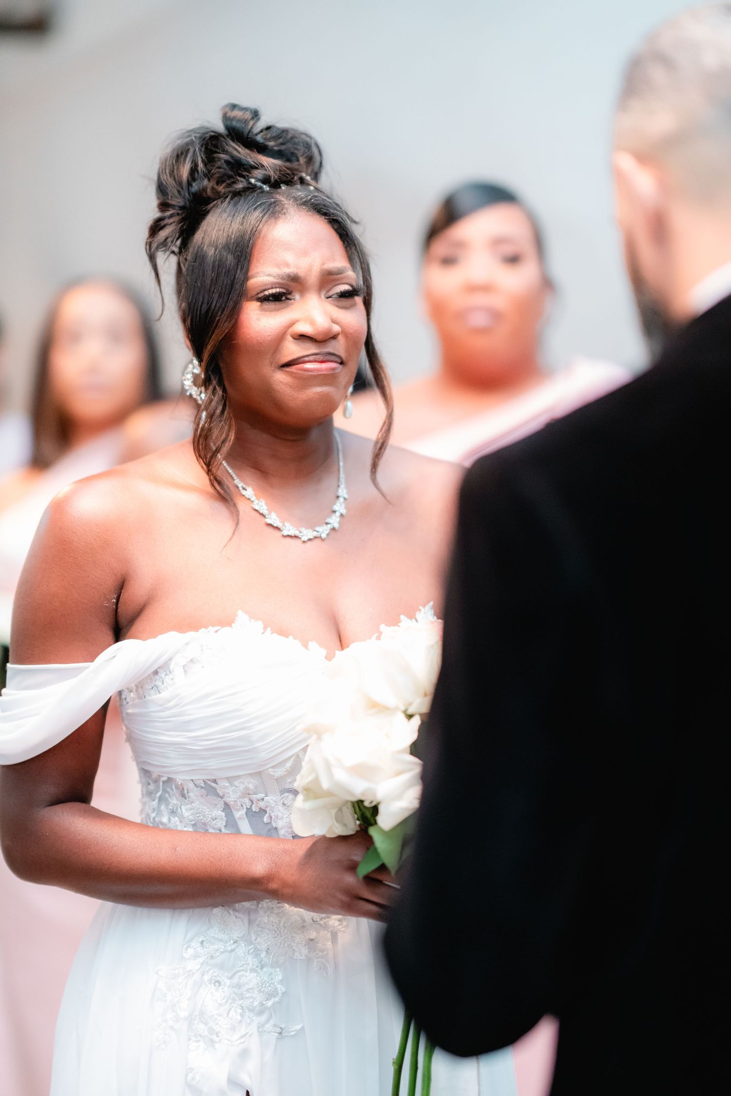 Intimate wedding ceremony moment captured with bride in off-shoulder gown holding white bouquet.