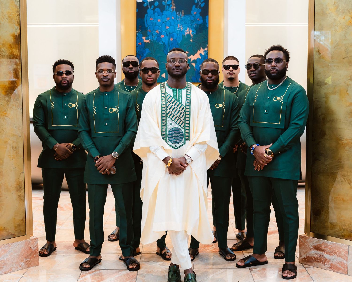 Groomsmen in matching green suits pose with the groom wearing a white traditional agbada.